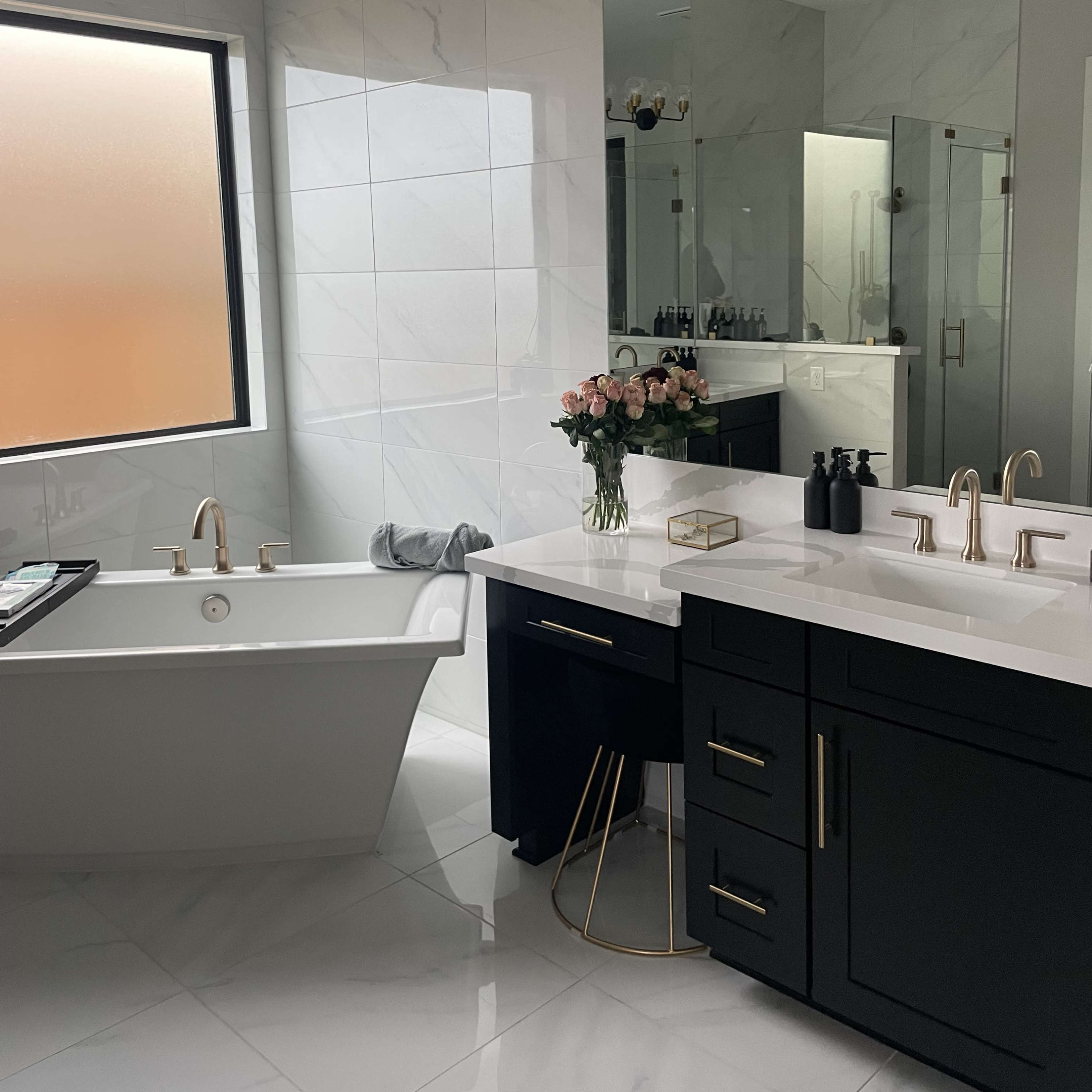 A modern bathroom features a freestanding bathtub, a dual sink vanity with dark cabinetry, and a large mirror, all illuminated by a chandelier.