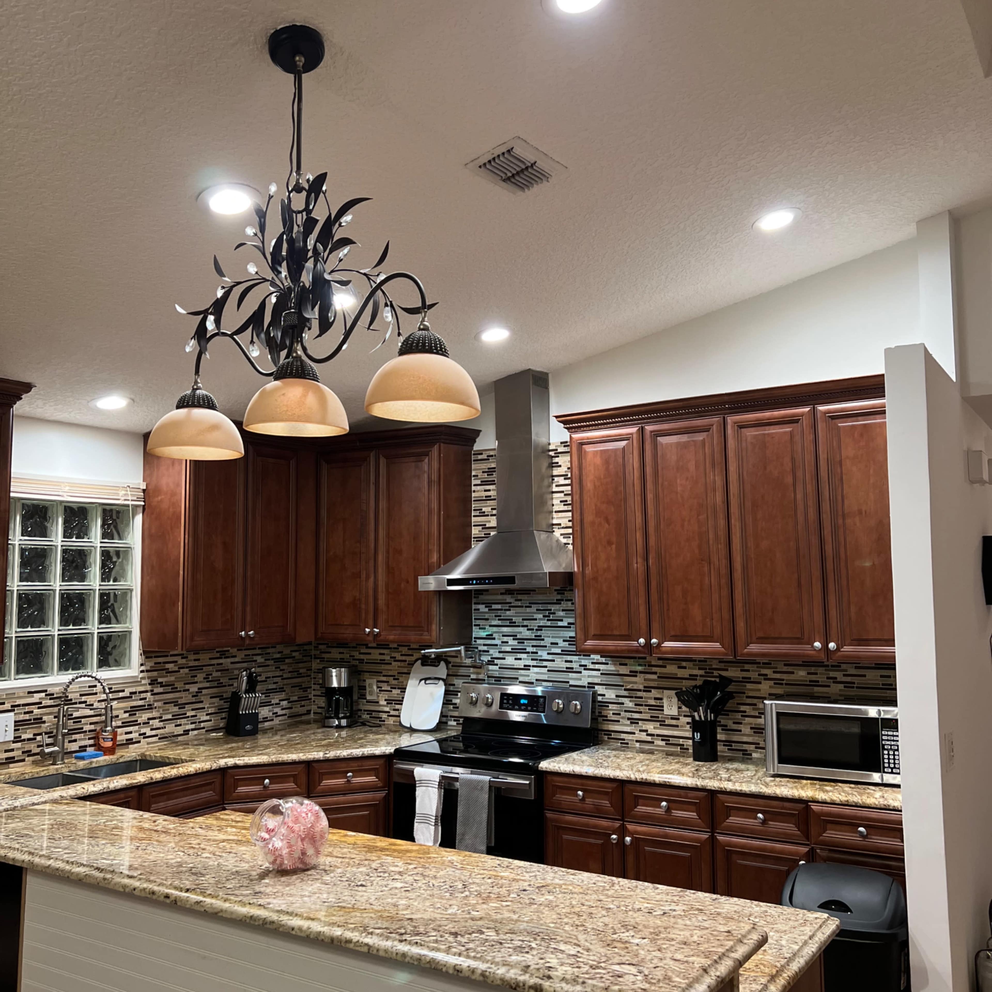 A modern kitchen with wooden cabinets, a granite countertop, stainless steel appliances, and a decorative chandelier.