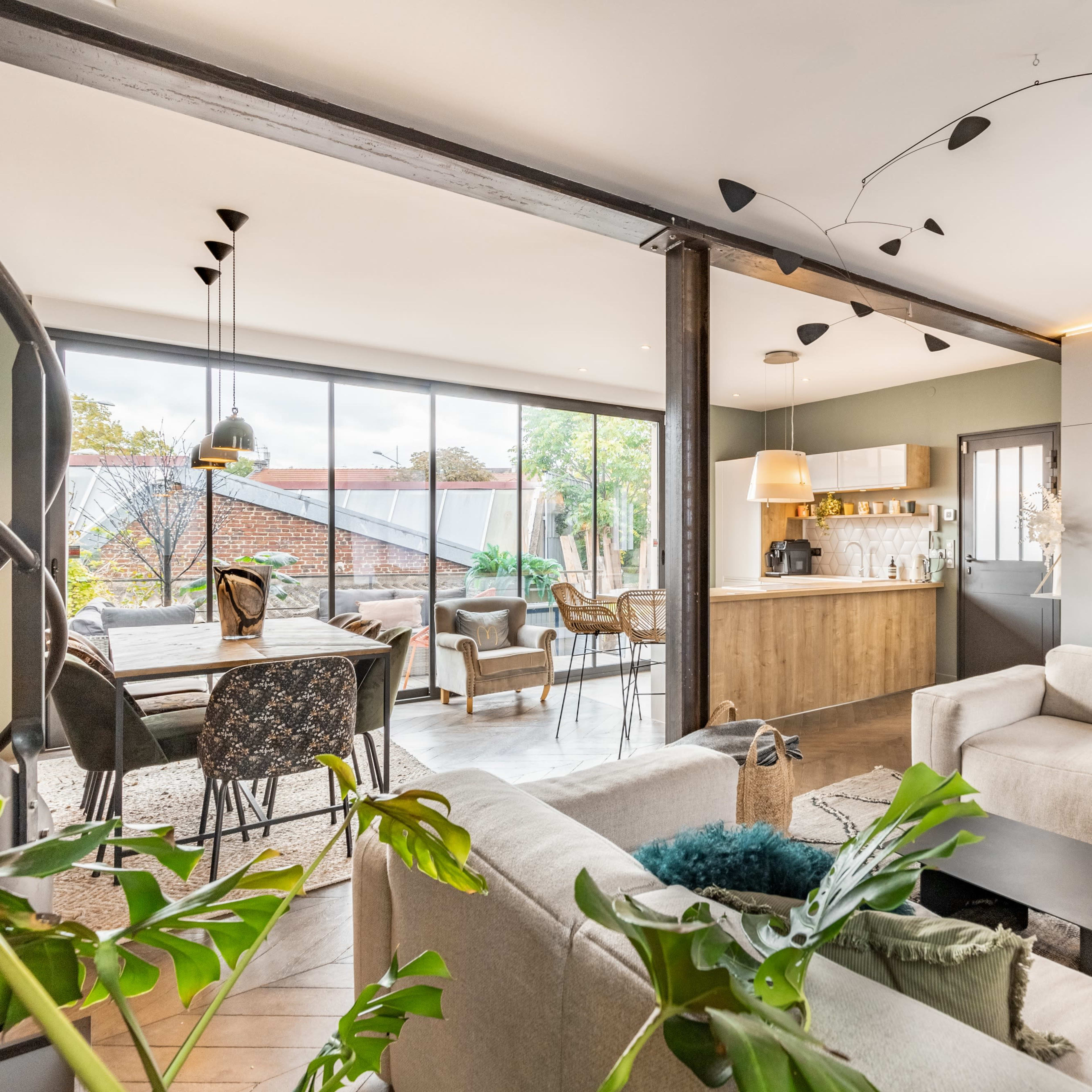 A modern living space featuring a light-colored sofa, a black coffee table, and a kitchen area visible in the background through large windows.