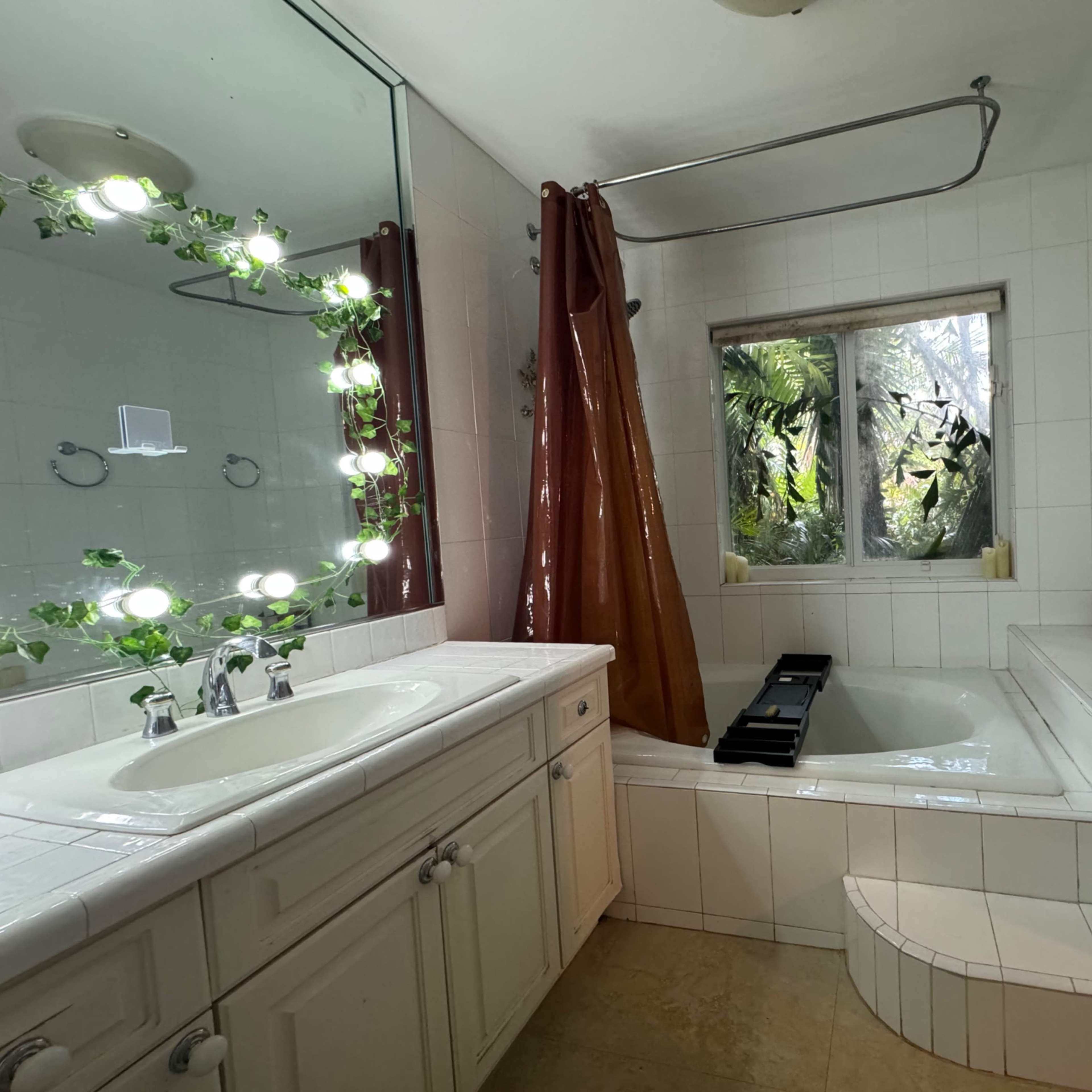 The bathroom features a large bathtub, a dual sink vanity with a mirror, and a window surrounded by greenery.