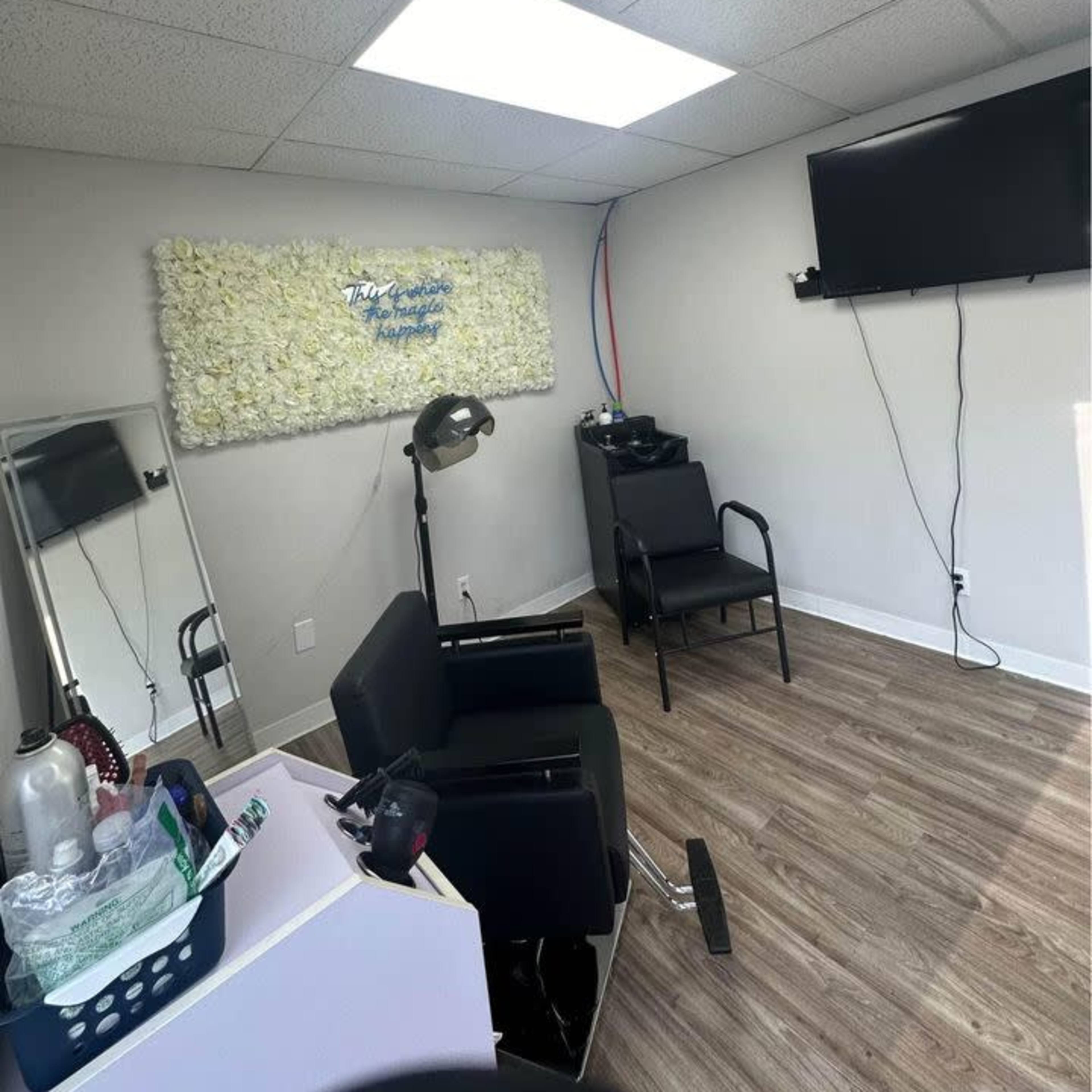 A salon chair positioned in a minimalistic room with a wall of faux flowers, a television mounted on the wall, and wooden flooring.
