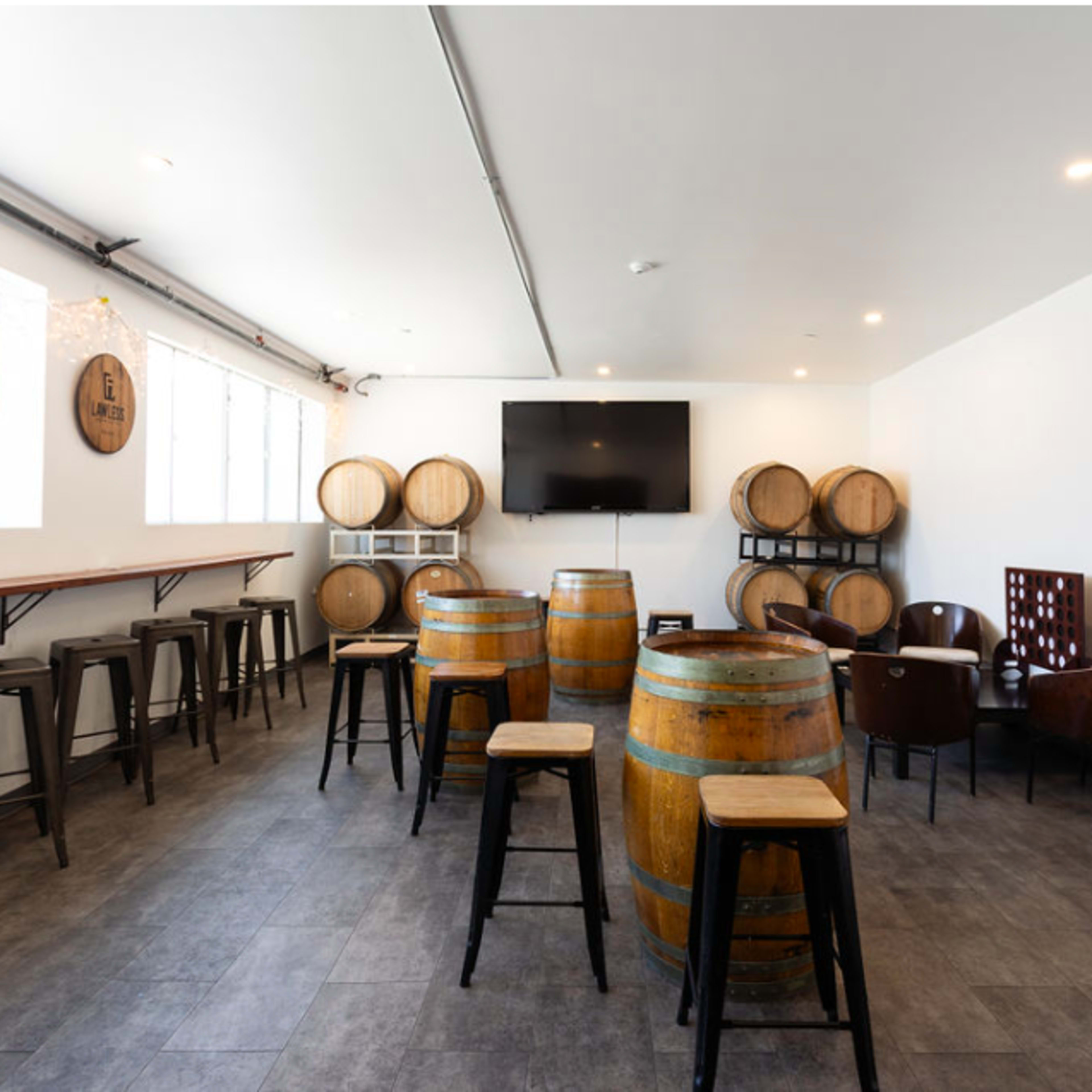 A spacious room with wooden barrels, seating tables, and chairs arranged around a wall-mounted television.