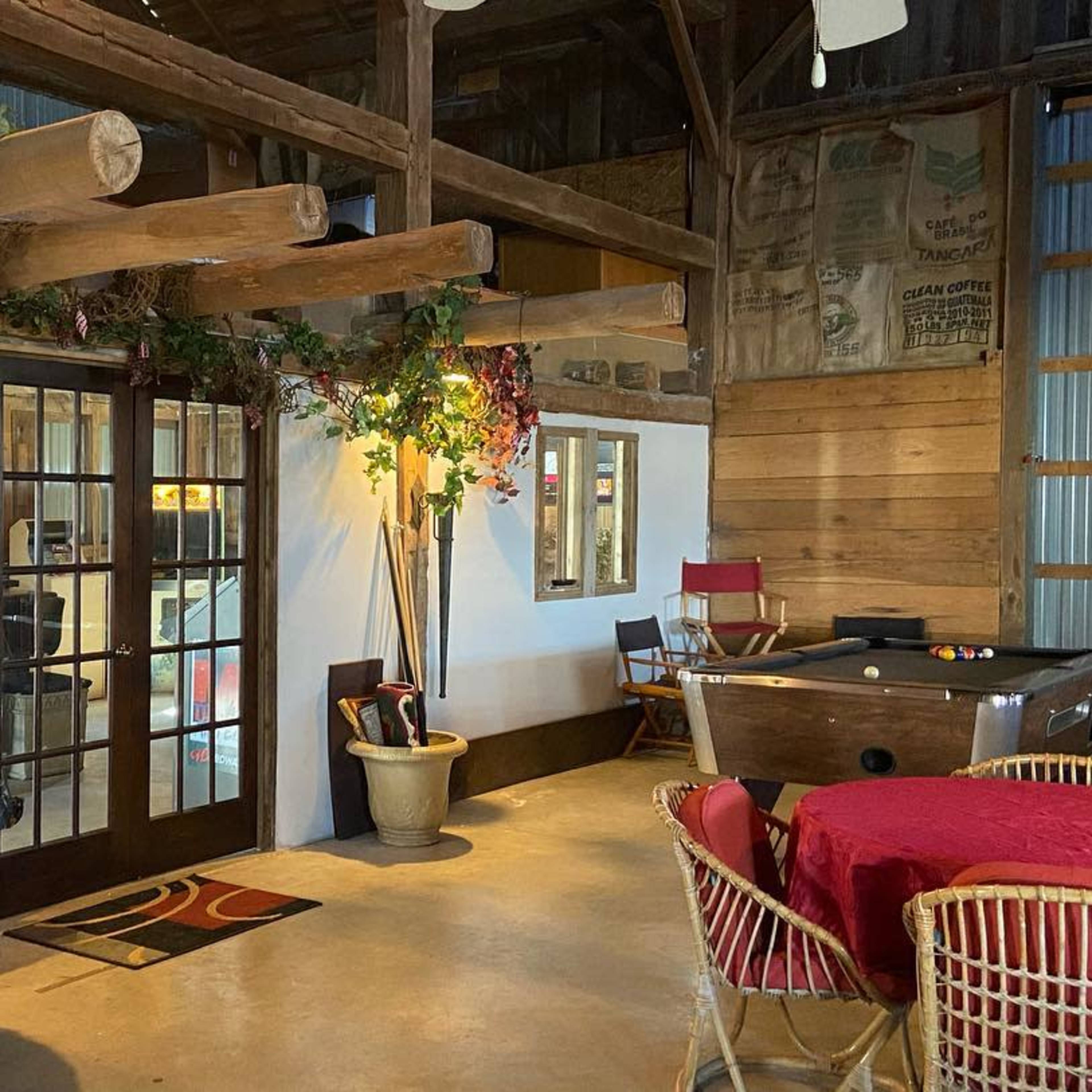 The interior of a rustic room features wooden beams, tables set with red linens, and a pool table in the corner.