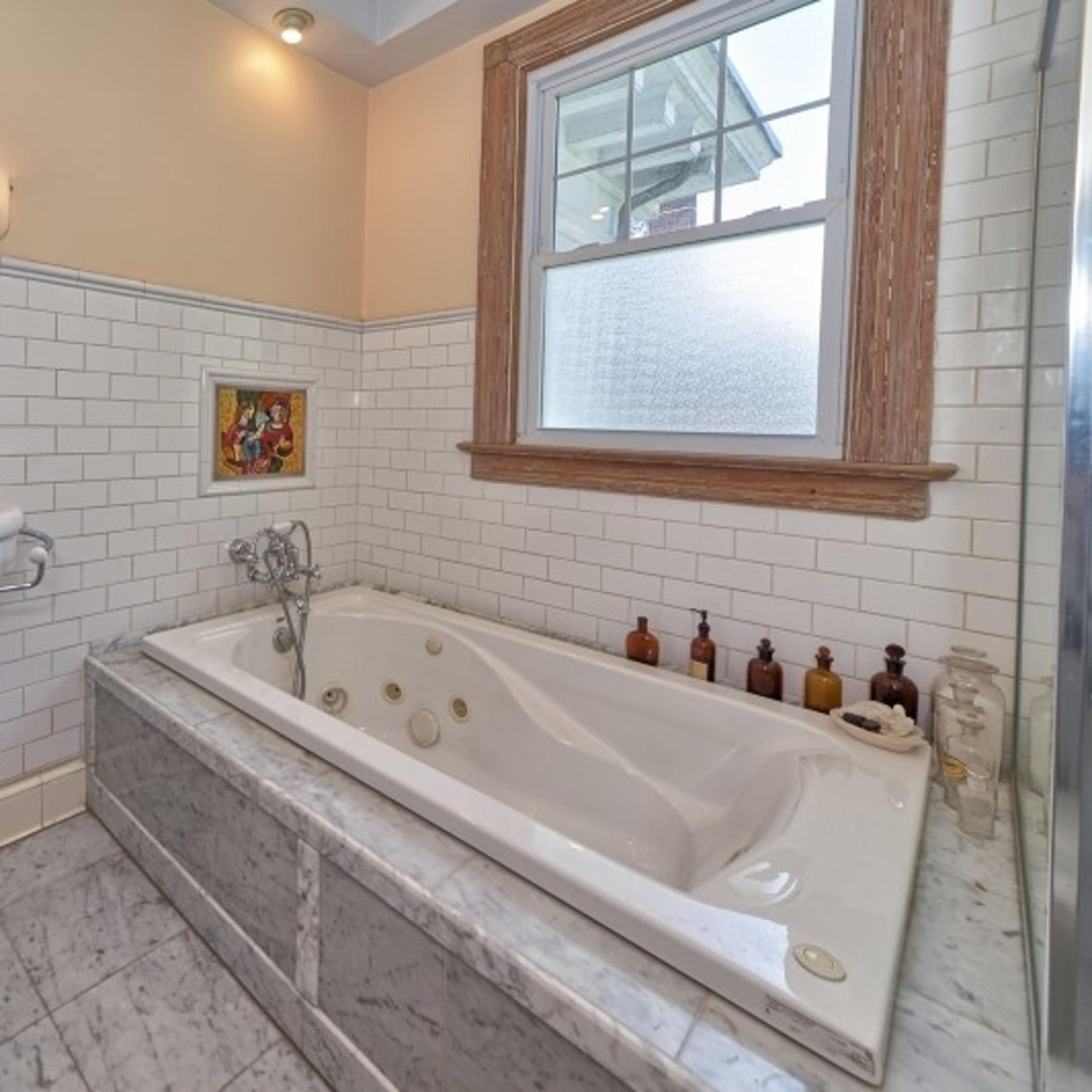 A bathroom featuring a freestanding sink, a jetted bathtub, and a large window.