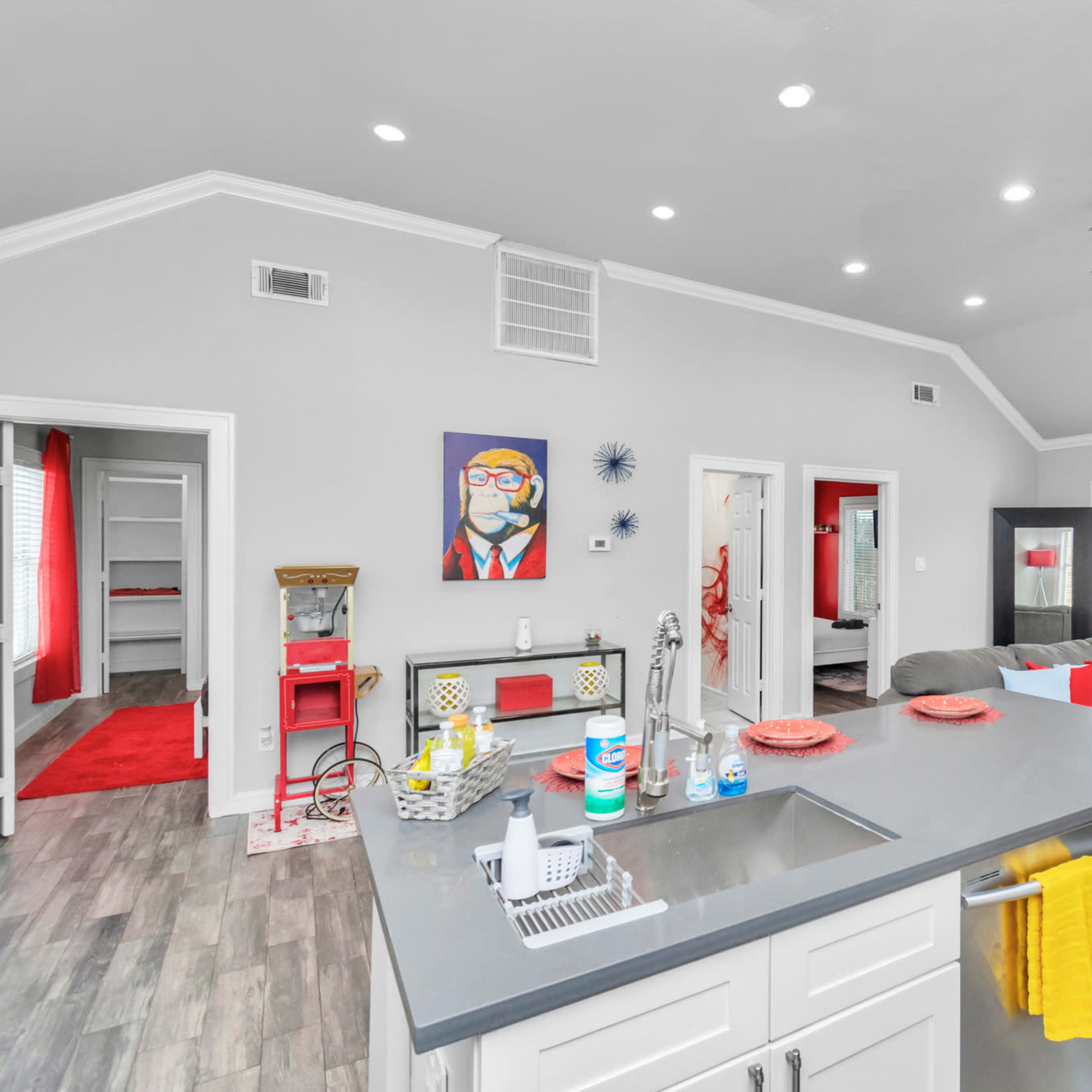 A modern open-concept living space featuring a kitchen island, a grey sectional sofa, colorful wall art, and bright accents in the decor.