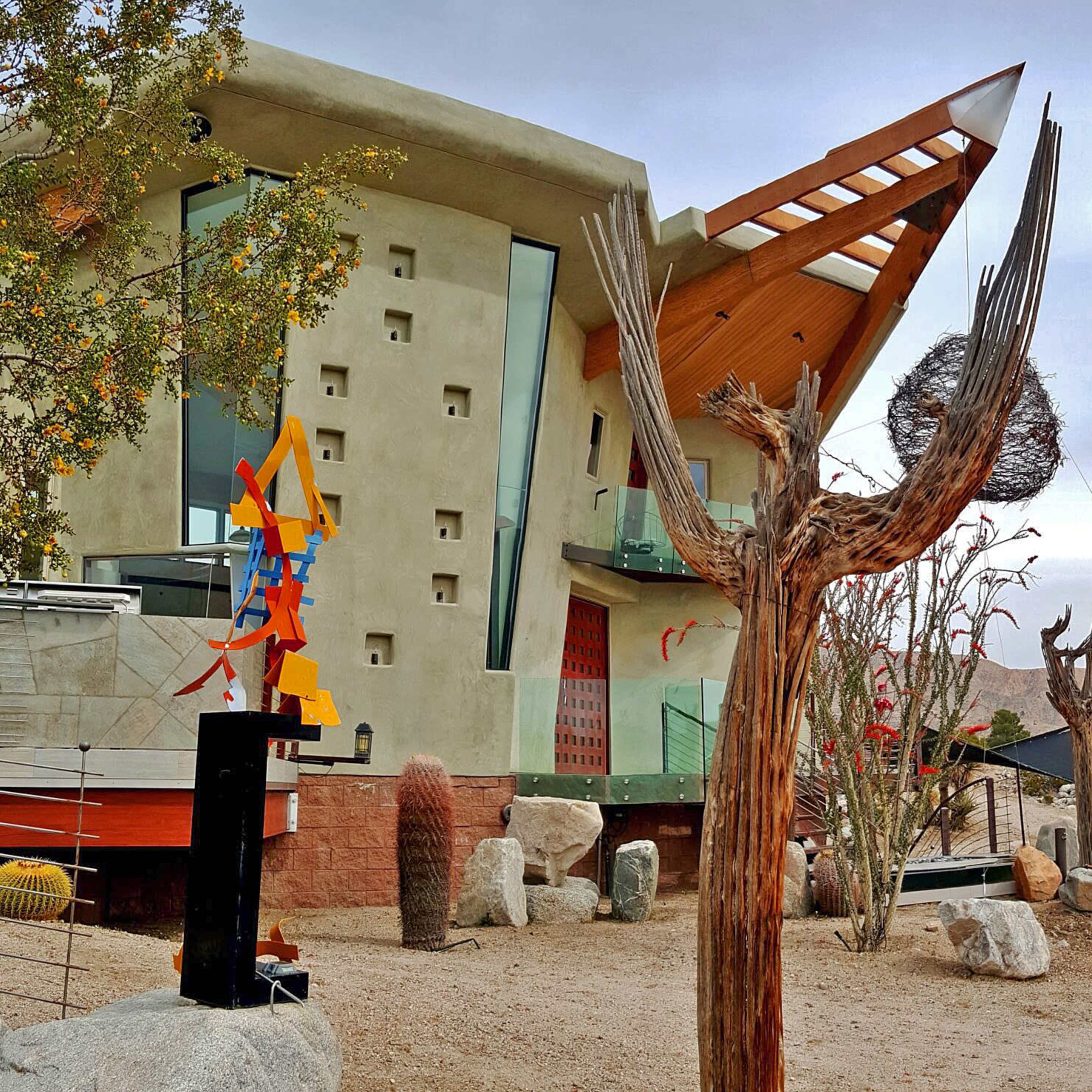 A modern building with an angular design surrounded by desert landscaping, including unique sculptures and native plants.