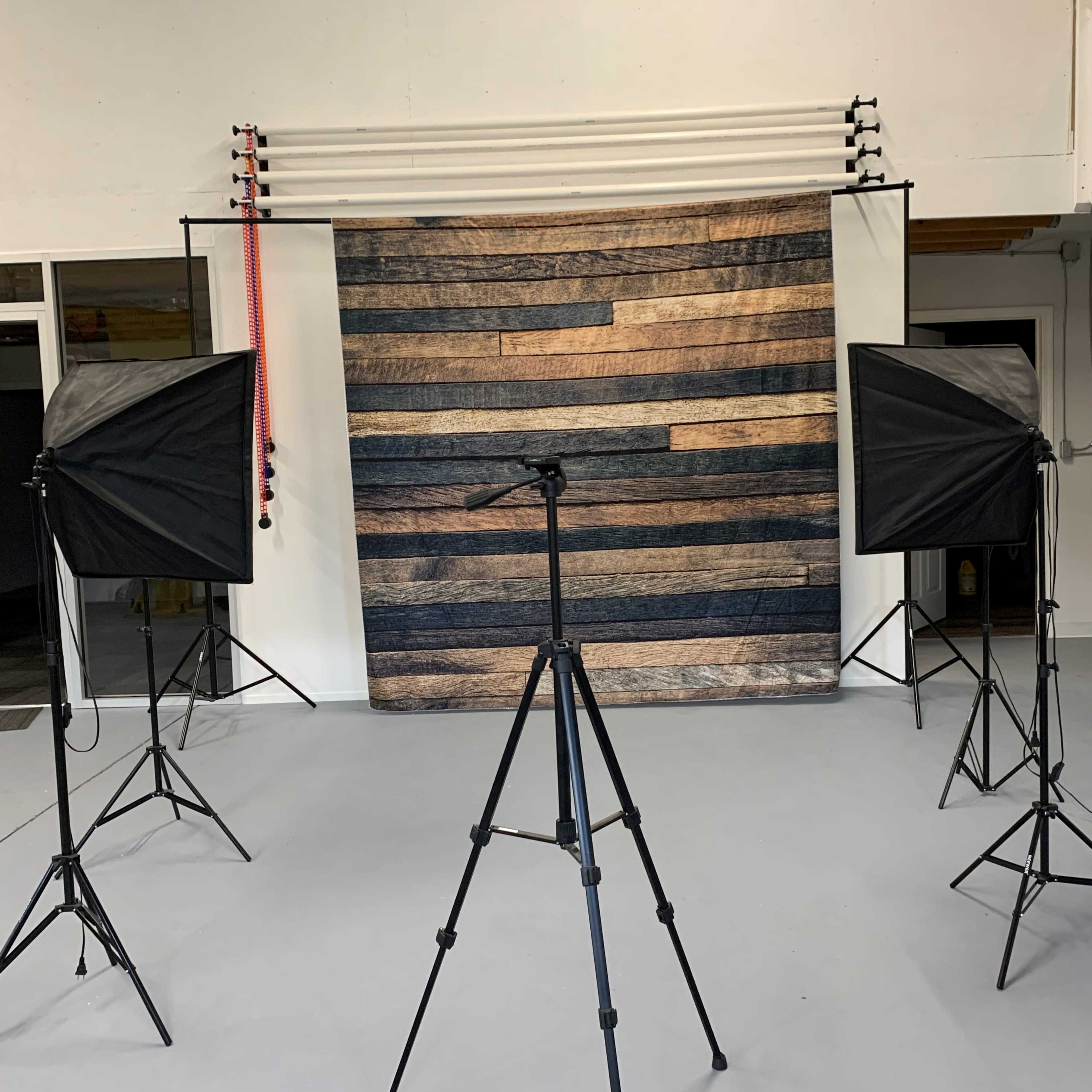 A photography studio setup with two softbox lights and a tripod facing a striped backdrop made of wood planks.