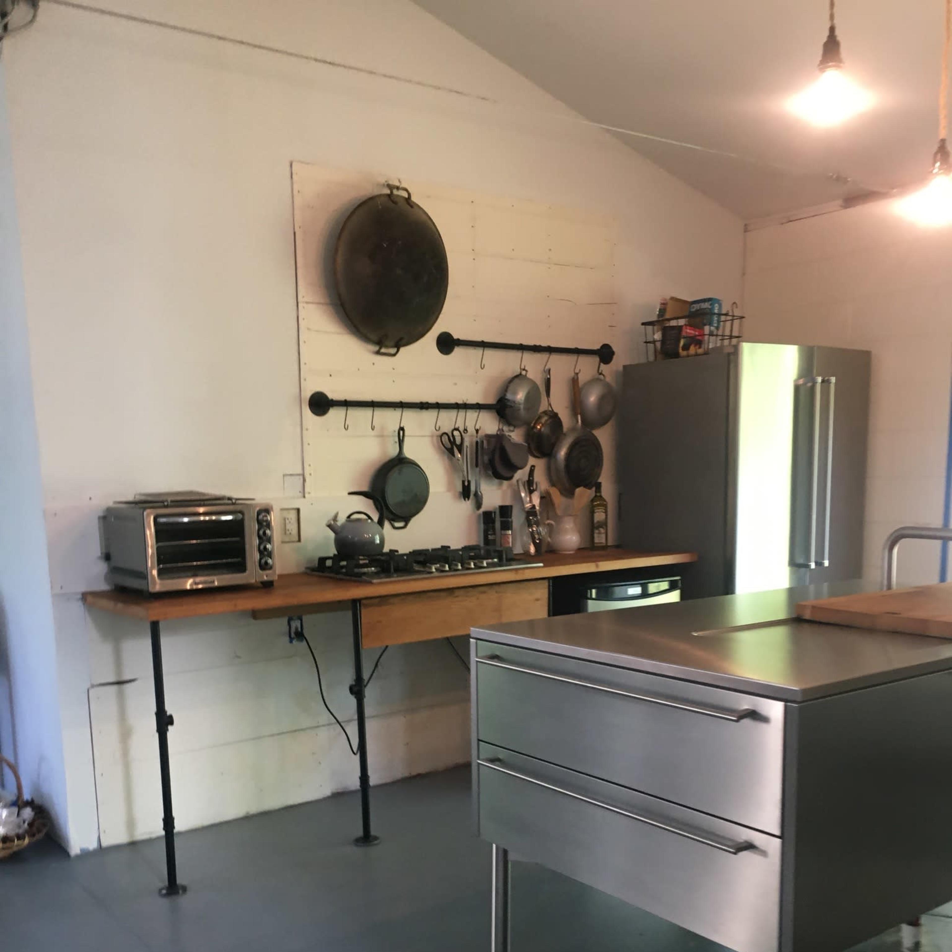 A minimalist kitchen with a wooden countertop, metal drawers, an oven, a cooktop, and various cooking utensils hanging on the wall.