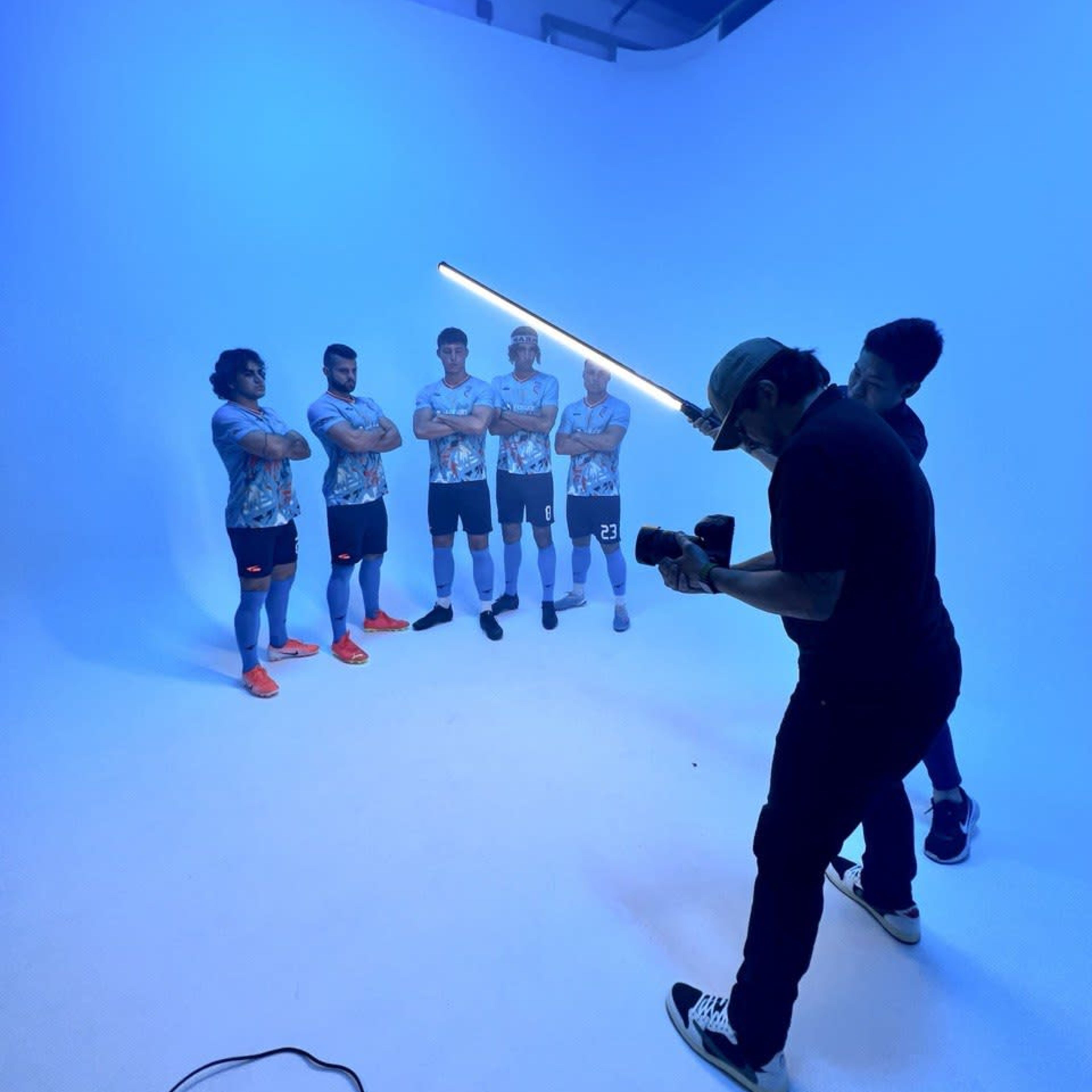 A photographer captures a group of six athletes posing under blue lighting in a studio setting.