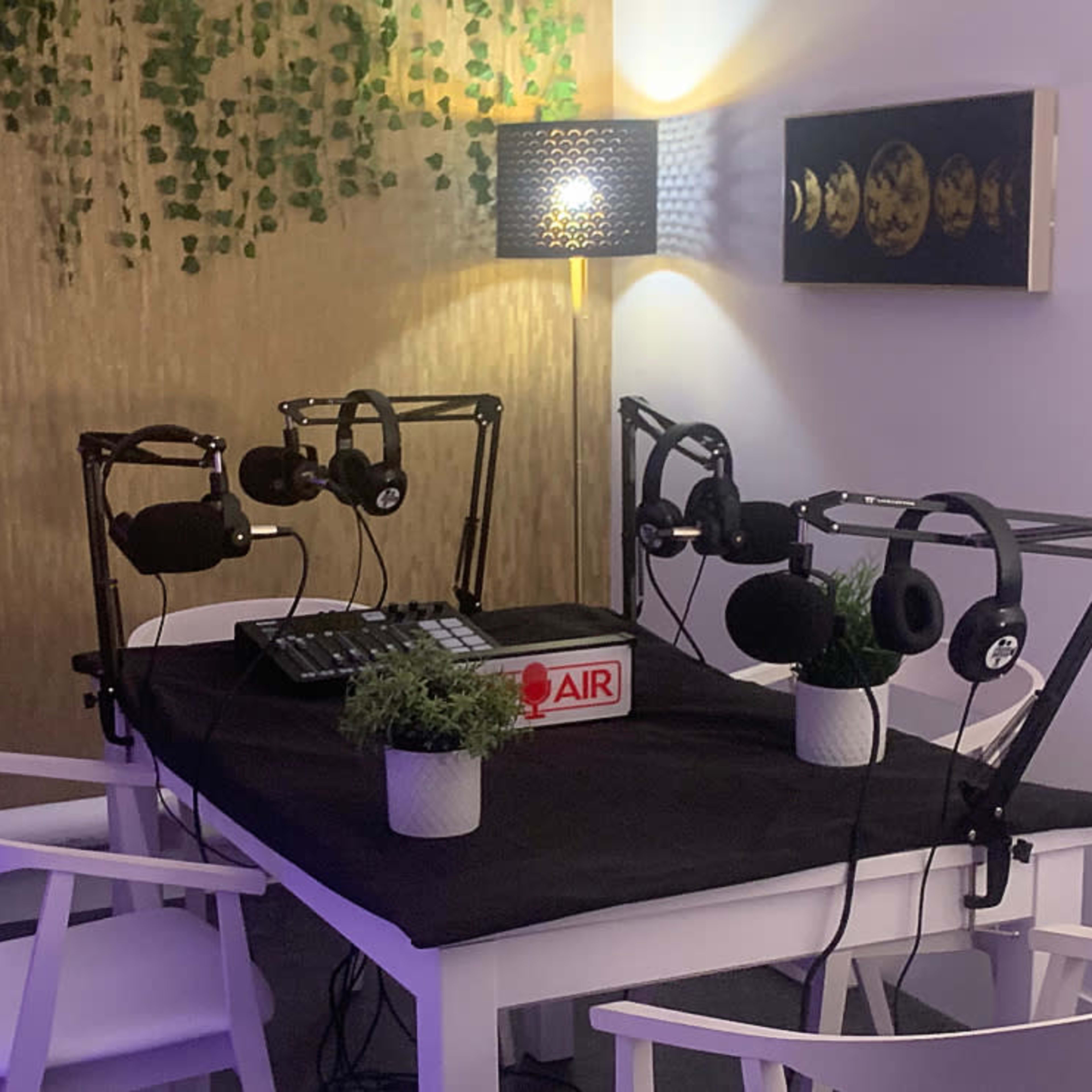 A podcast recording setup featuring a table with microphones, headphones, and a sound mixer, surrounded by decorative plants and soft lighting.