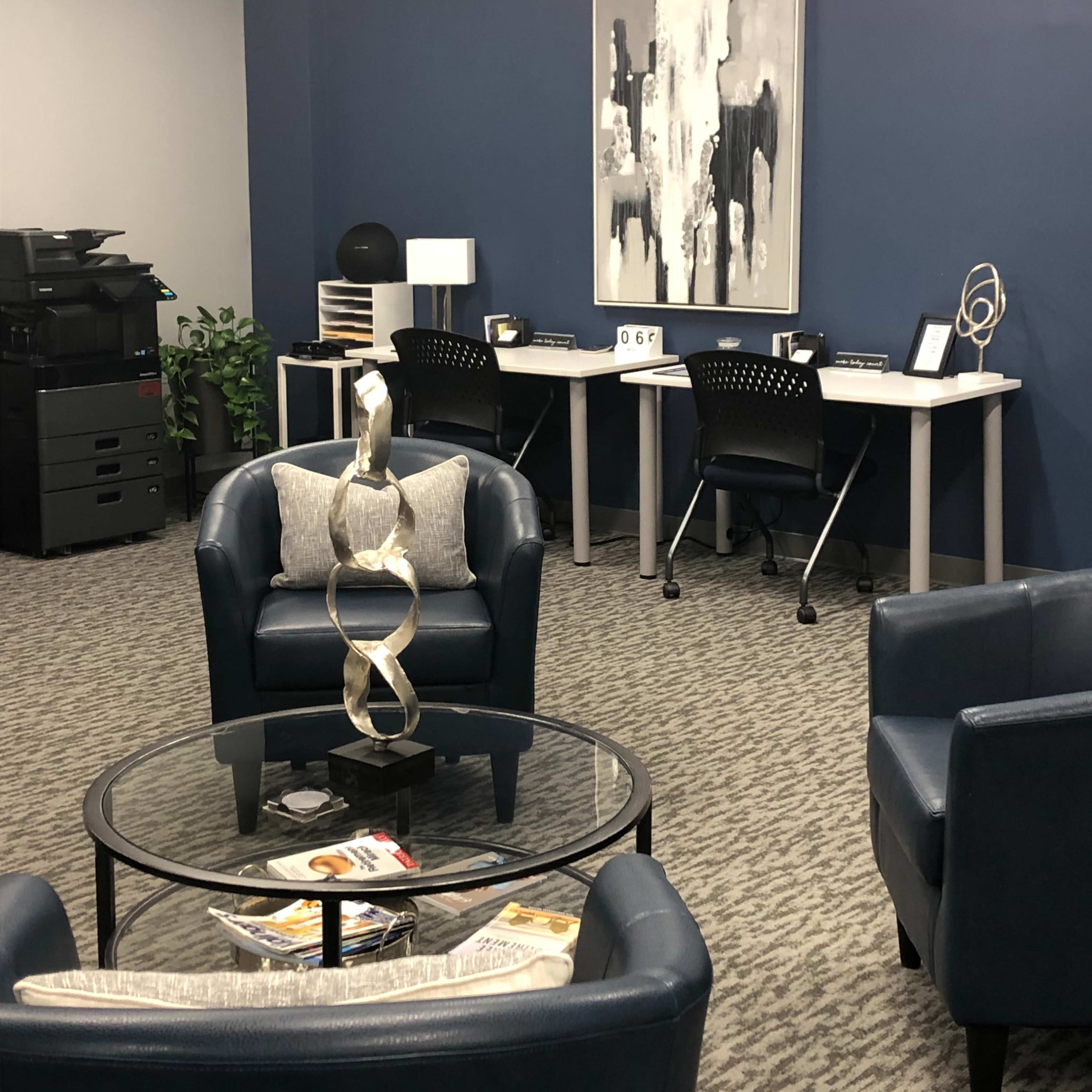 A modern office space with two desks, a coffee table, and seating arranged around the area.