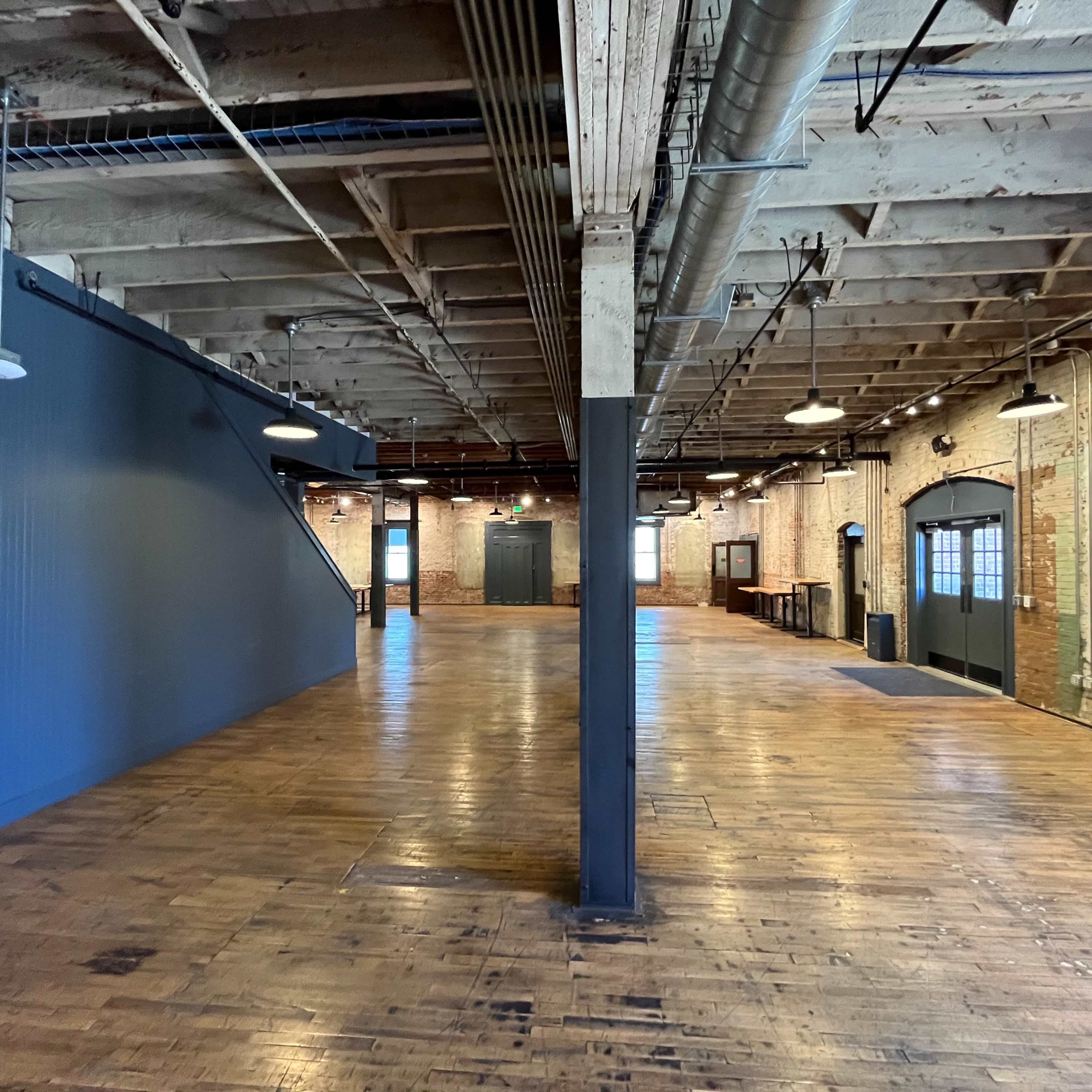 A spacious, industrial-style interior with wooden floors, exposed brick walls, and overhead lights.