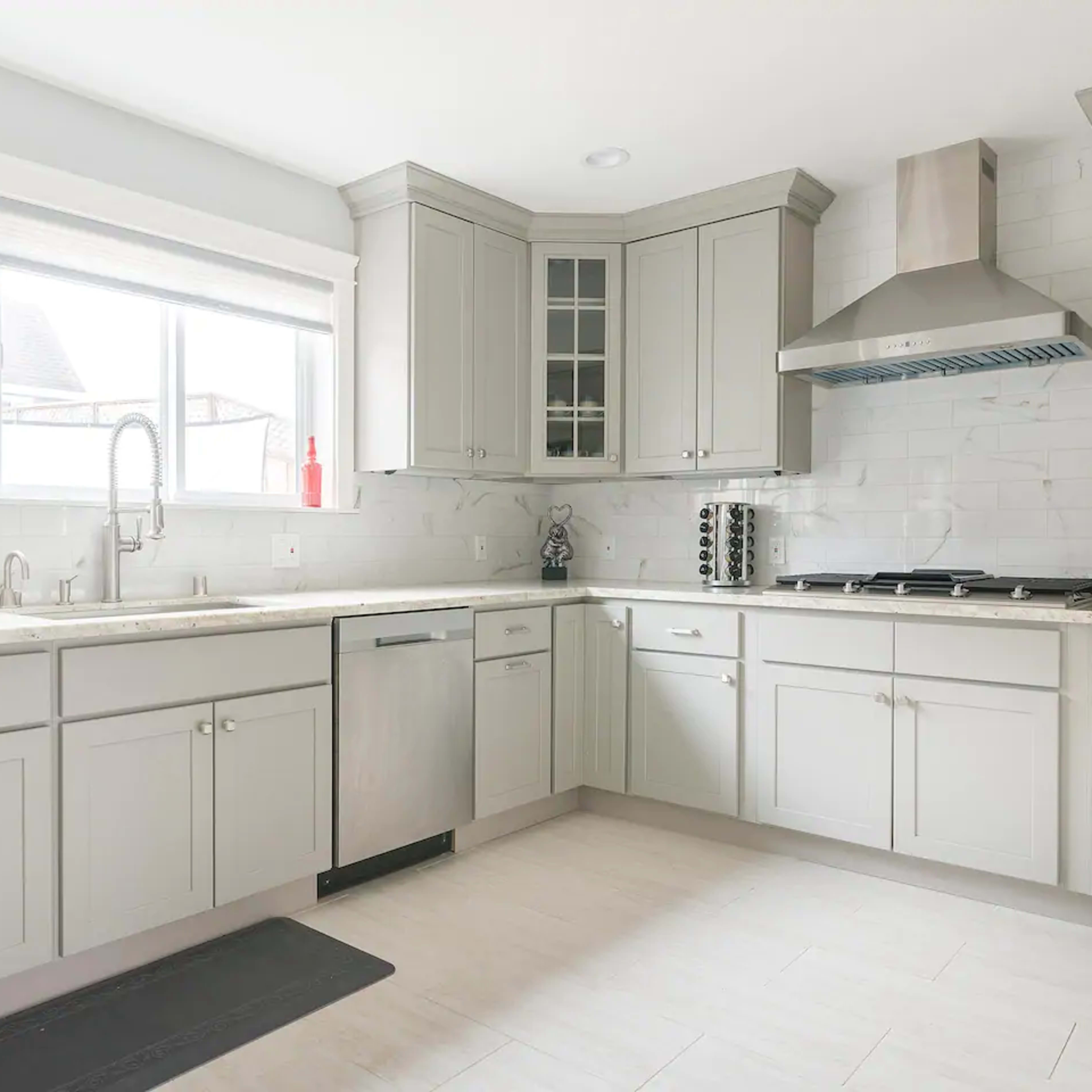 A modern kitchen features light gray cabinets, a stainless steel dishwasher, and a gas stove under a stainless steel range hood.
