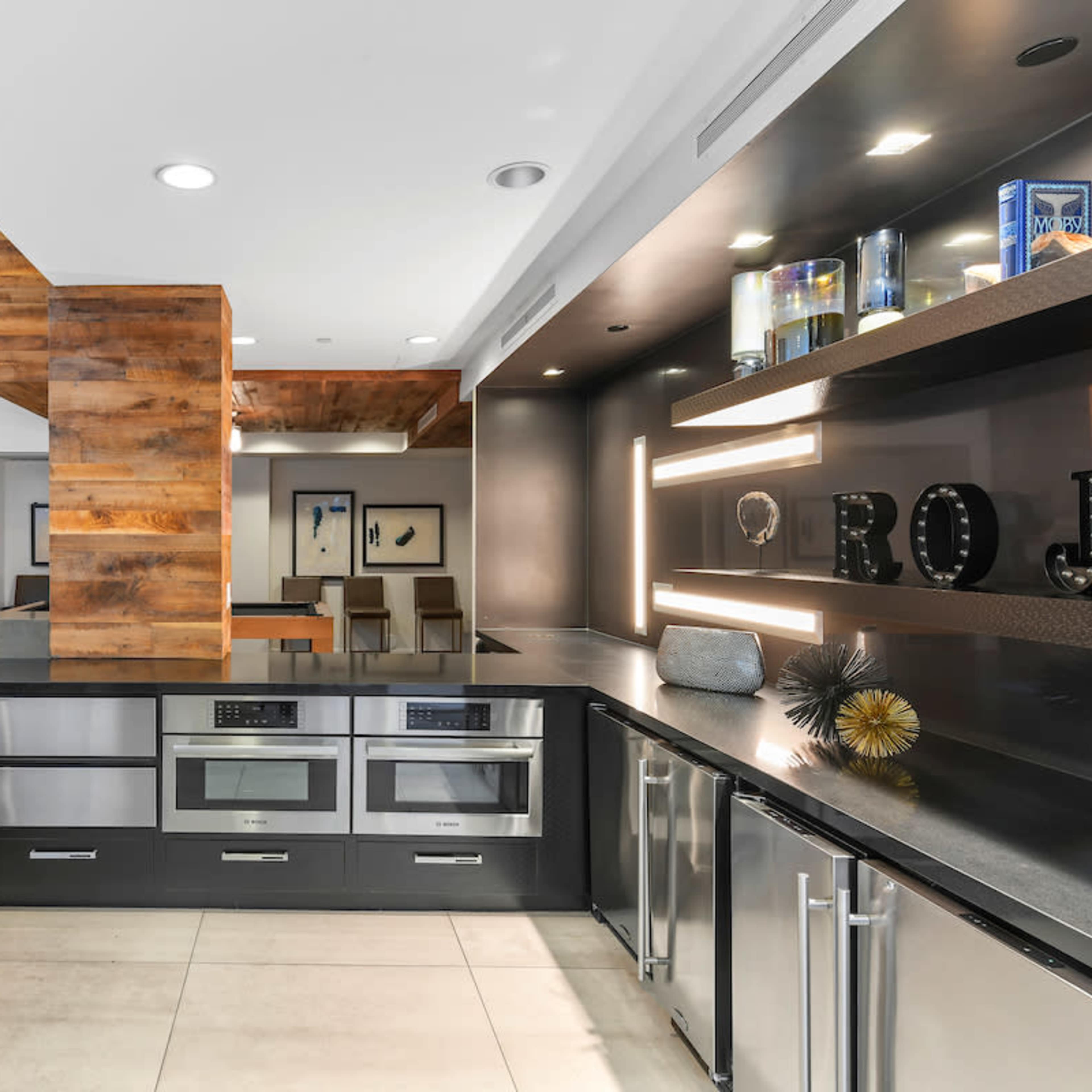 A modern kitchen with dark cabinetry, stainless steel appliances, and a large island counter.