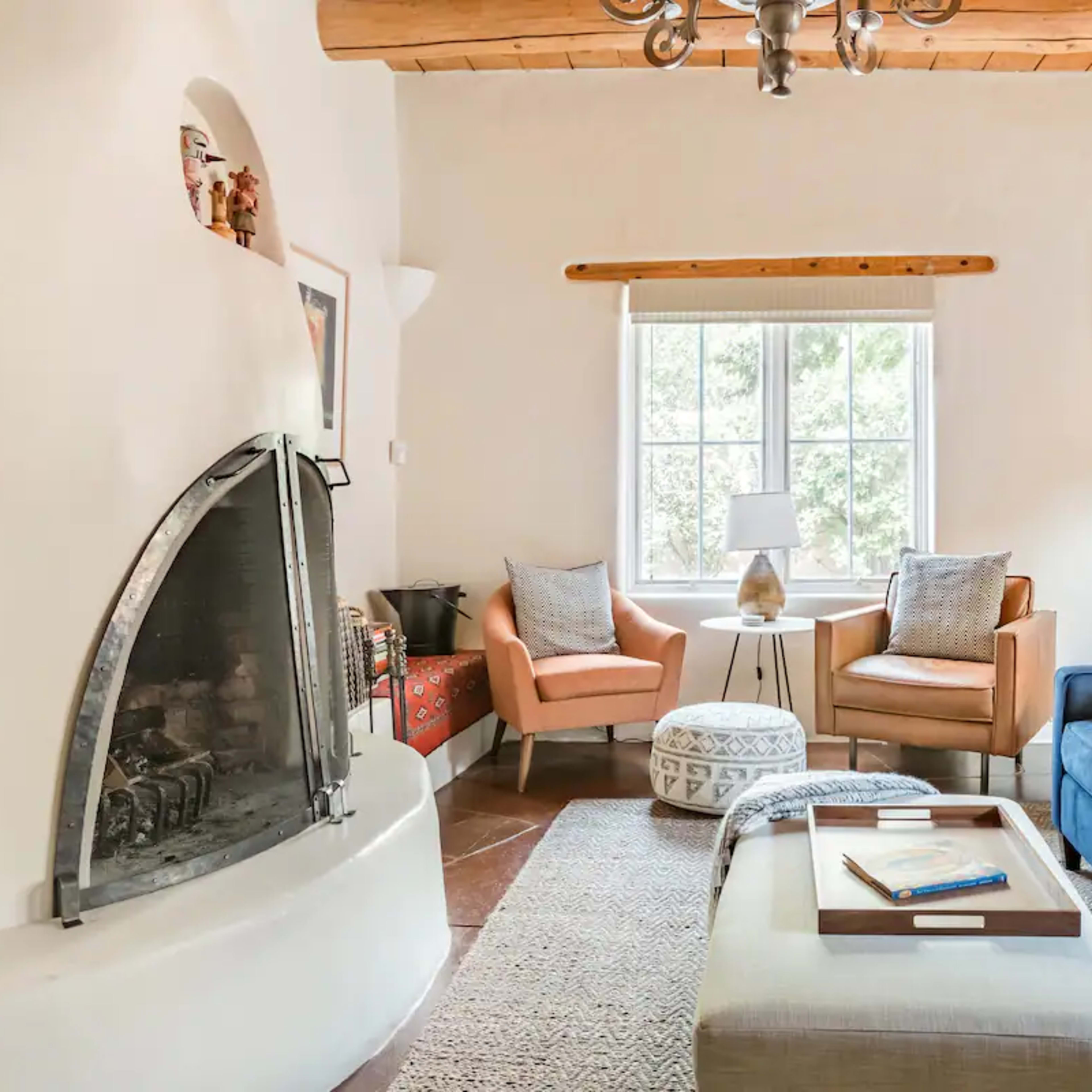 A cozy living room features a blue sofa, two seating chairs, a round ottoman, and a fireplace with a unique curved design.