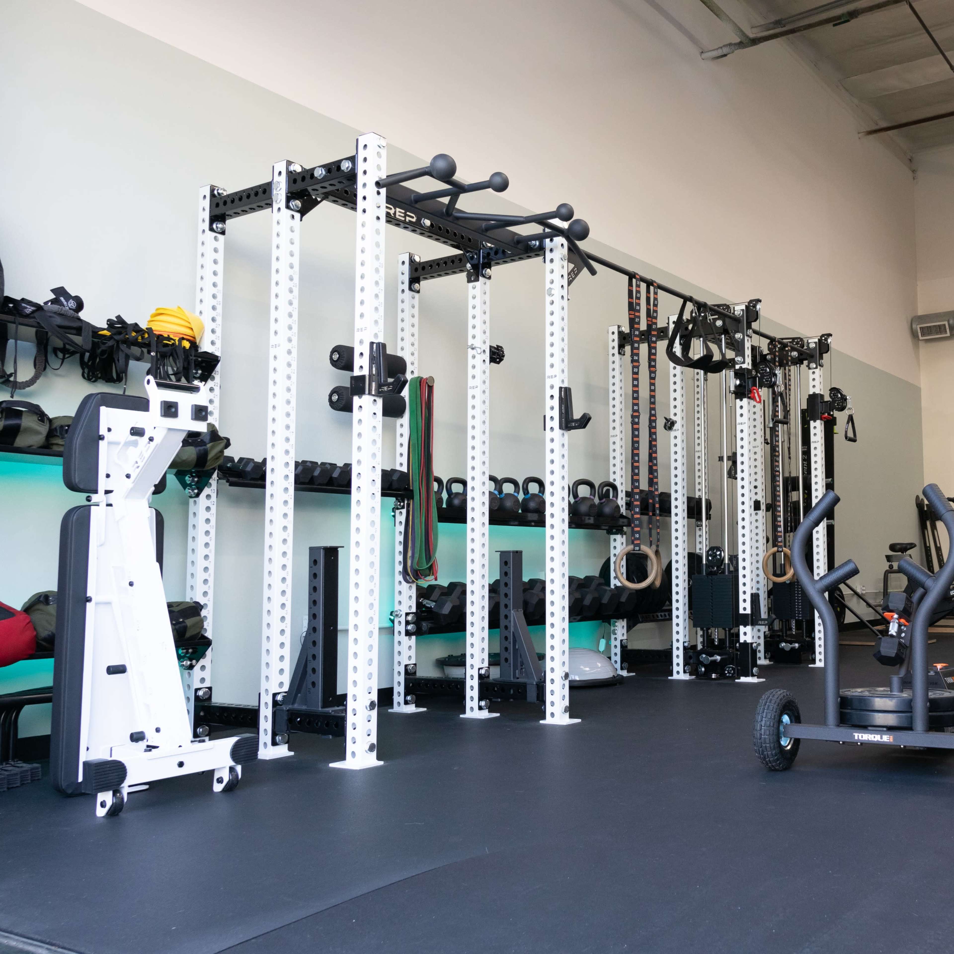 A well-equipped gym featuring a functional training rig, exercise equipment, and weights arranged on shelves.