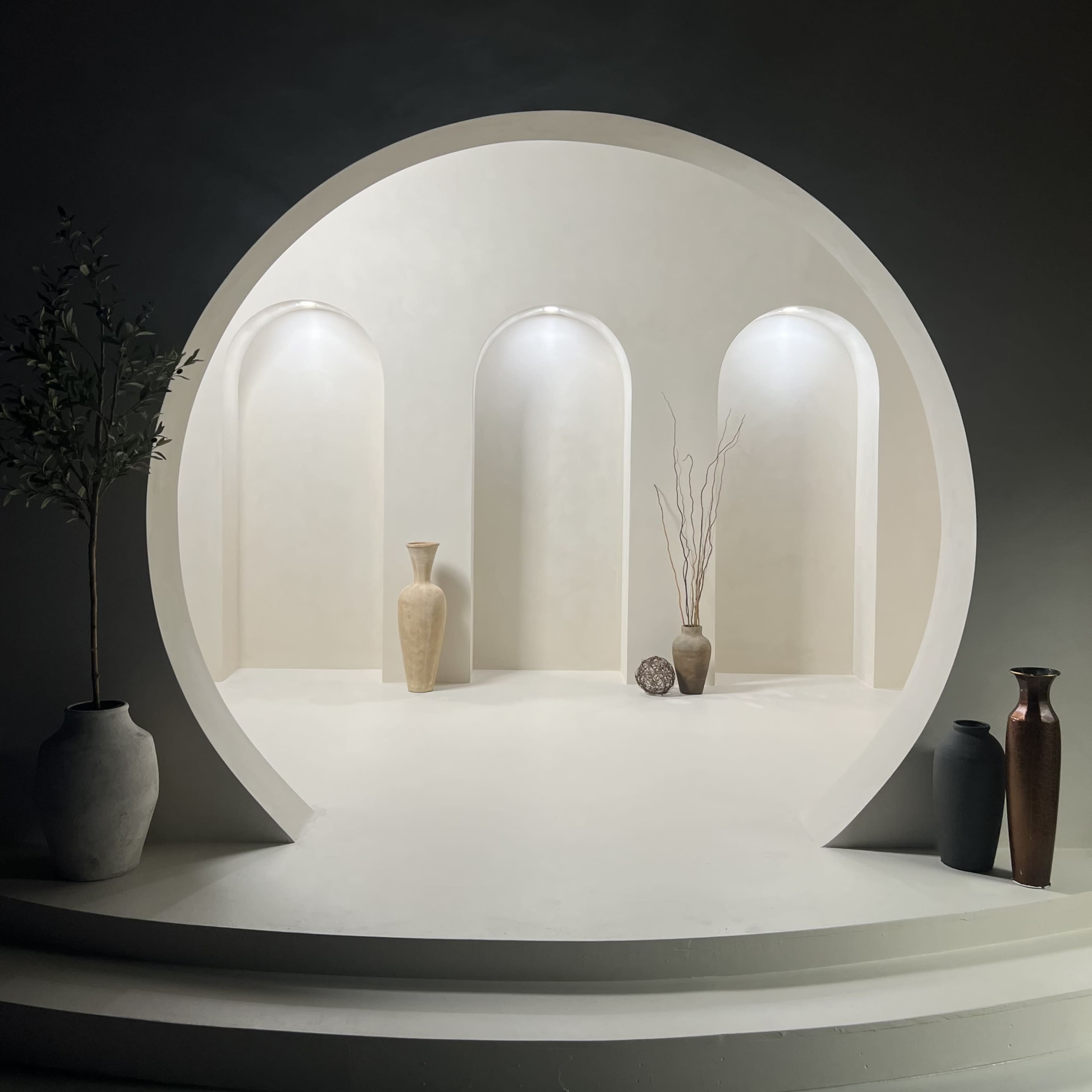A minimalist display niche with three arched alcoves, two vases, and decorative elements set against a softly illuminated background.