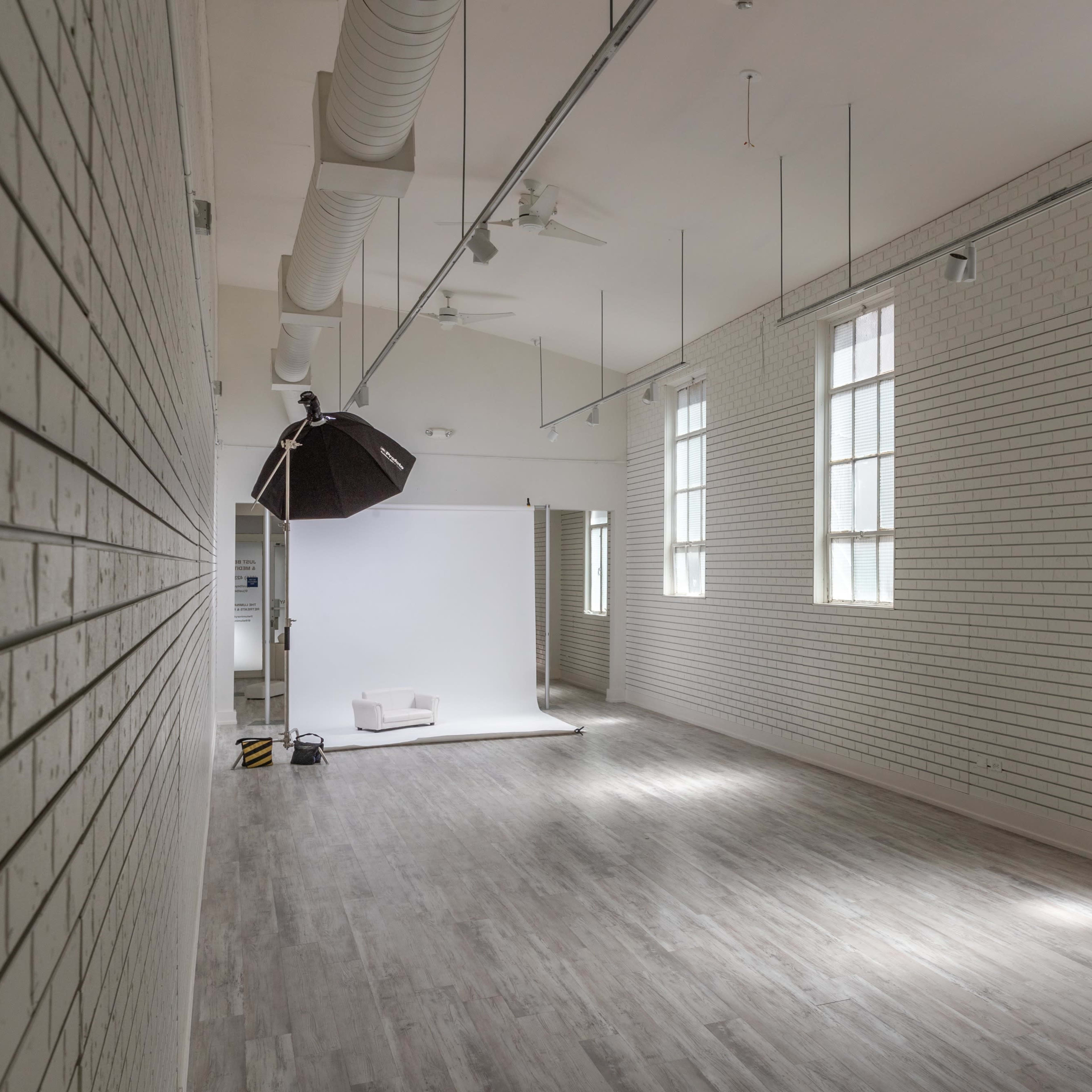 A spacious, well-lit photography studio with white brick walls and large windows.