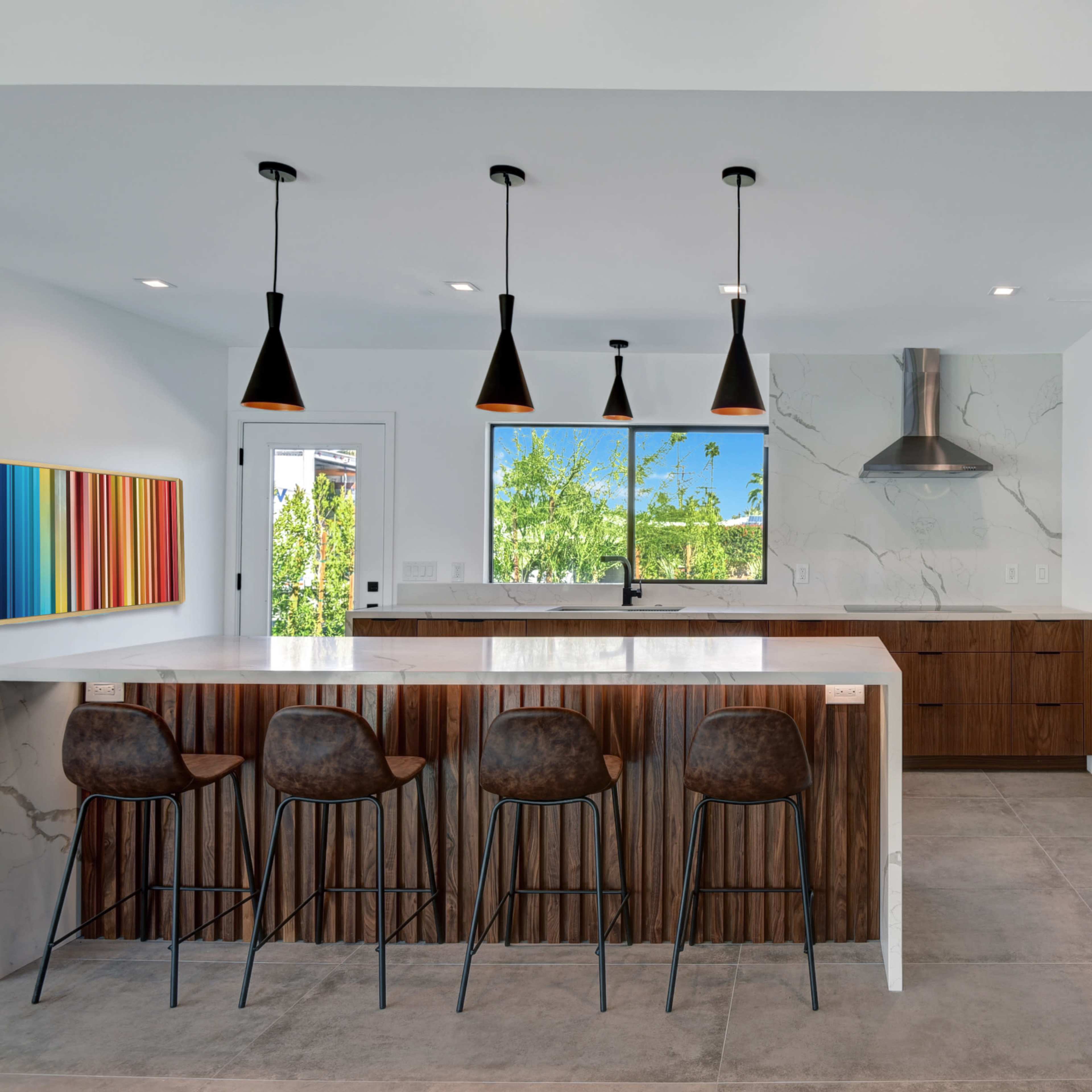 A modern kitchen features a large island with bar seating, sleek cabinetry, and prominent appliances alongside a window with a view.