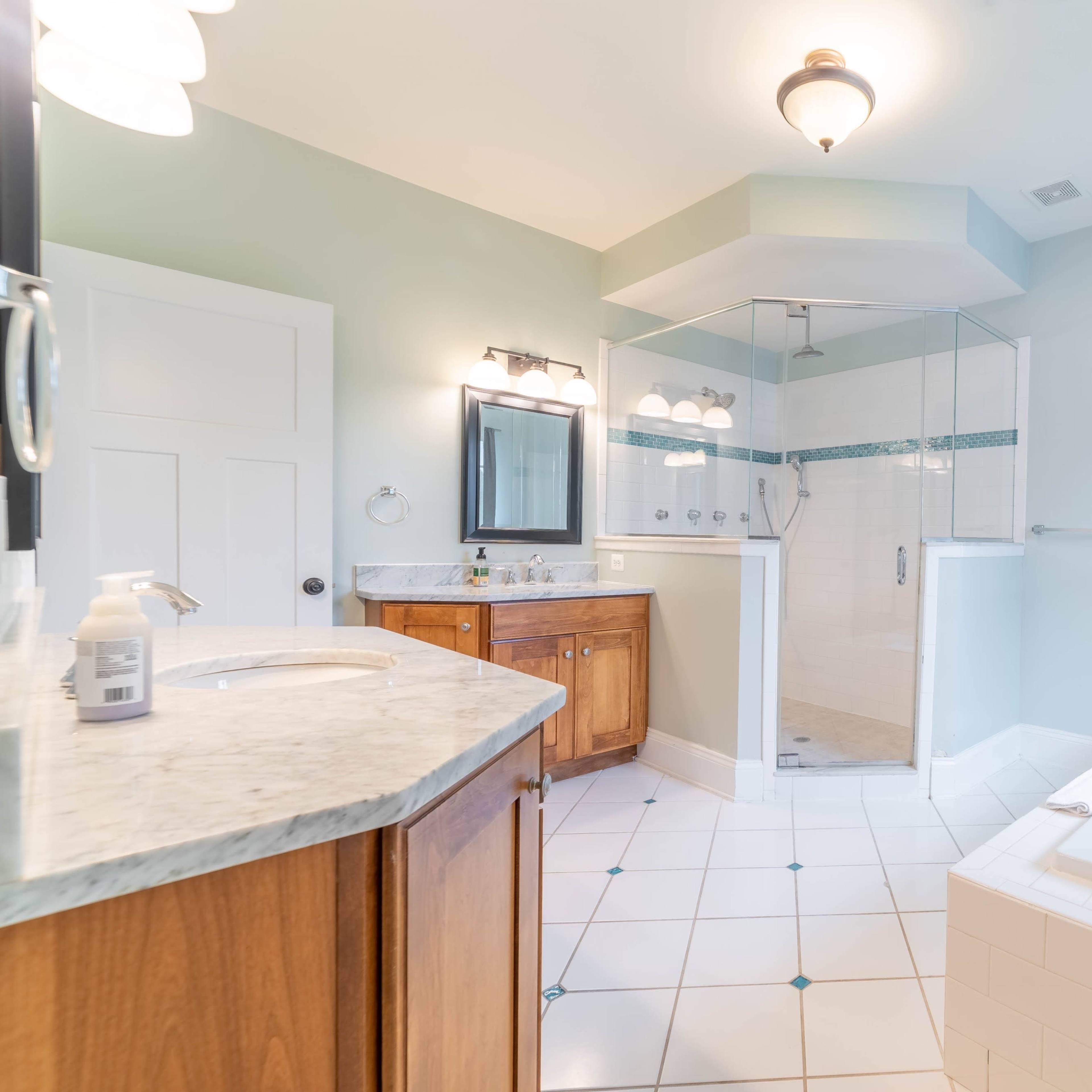 A spacious, well-lit bathroom featuring a glass-enclosed shower, a soaking tub, vanity with cabinets, and tile flooring.