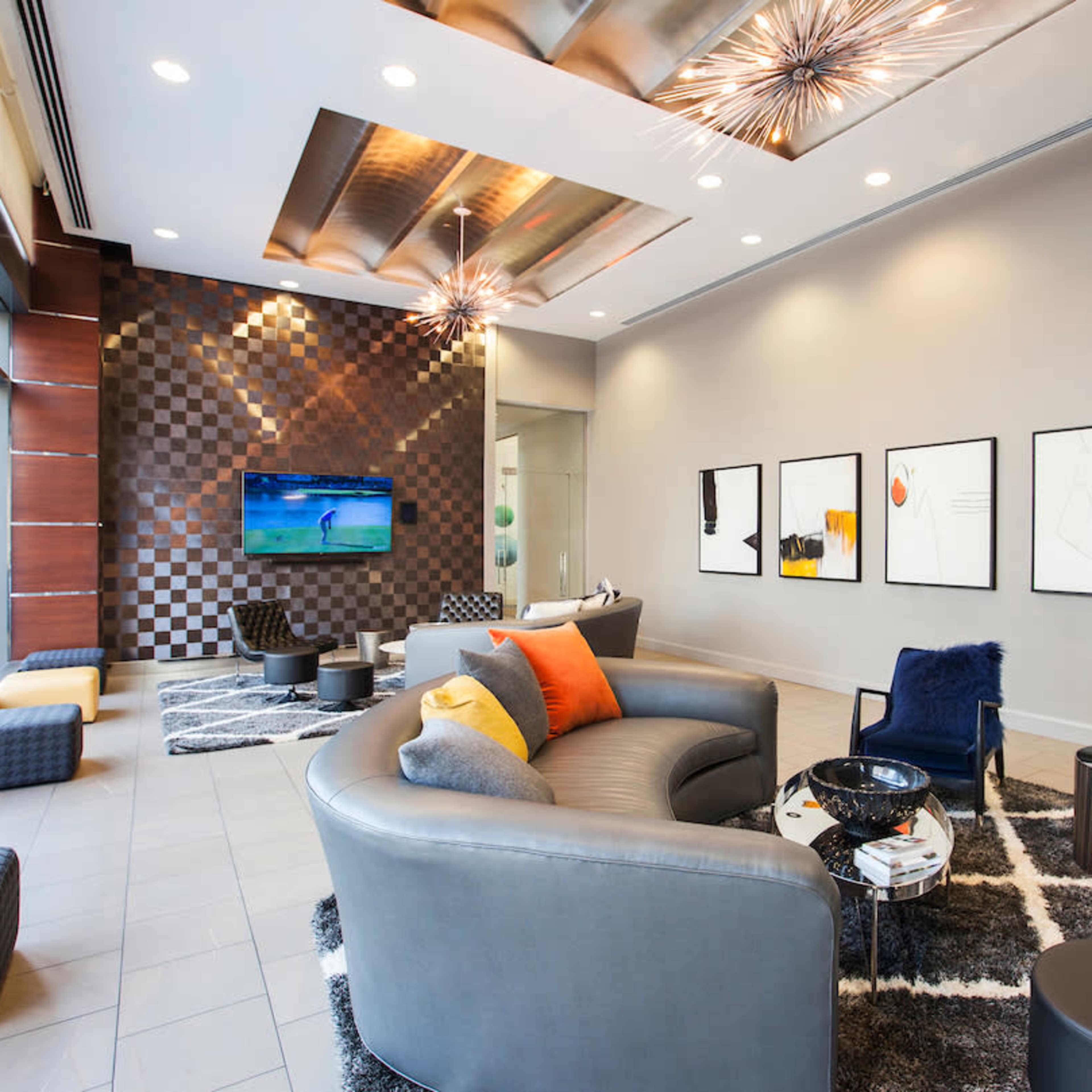 A modern lounge area featuring a television on the wall, various seating arrangements, and decorative artwork.