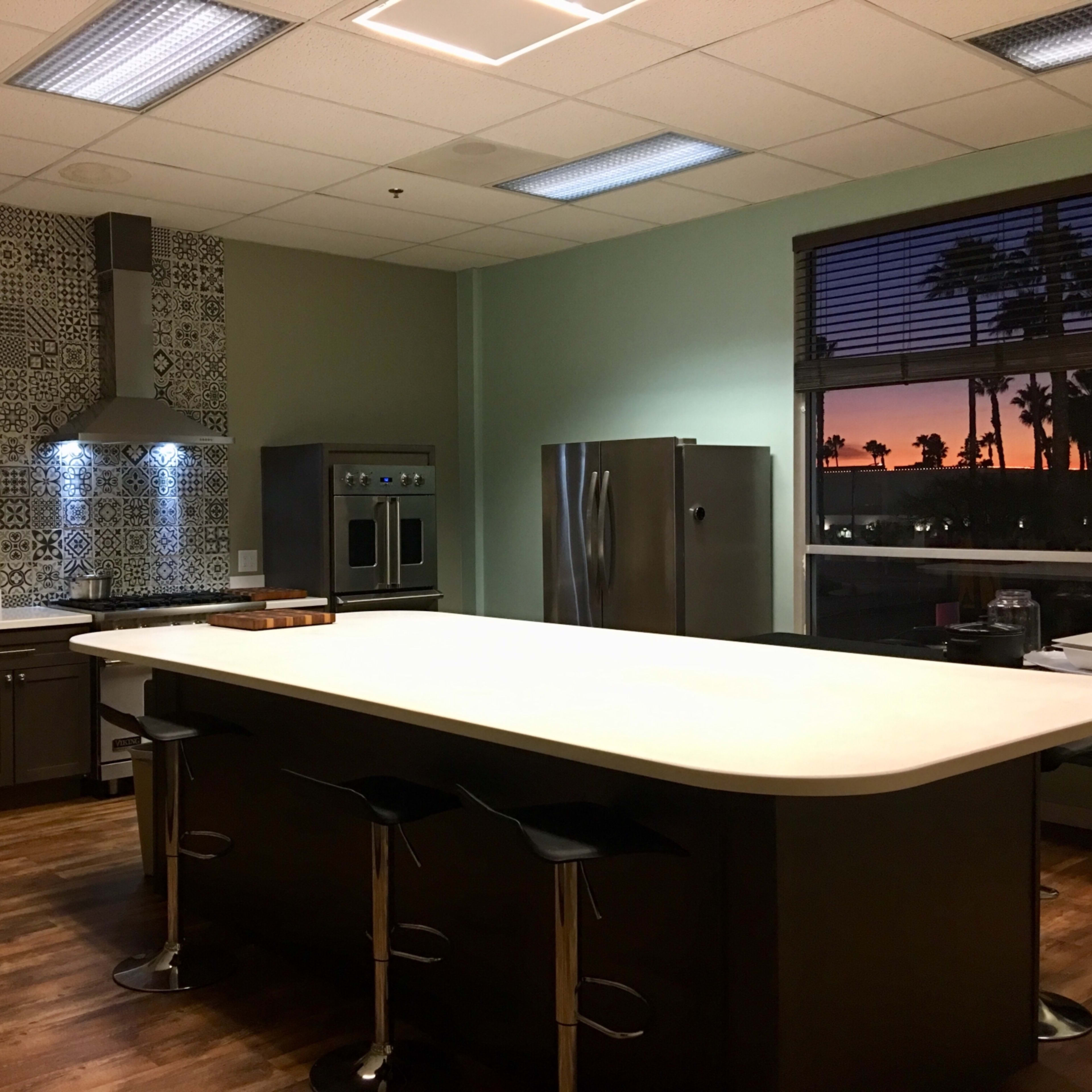 The kitchen features a large island with bar stools, stainless steel appliances, and a sunset visible through the window.