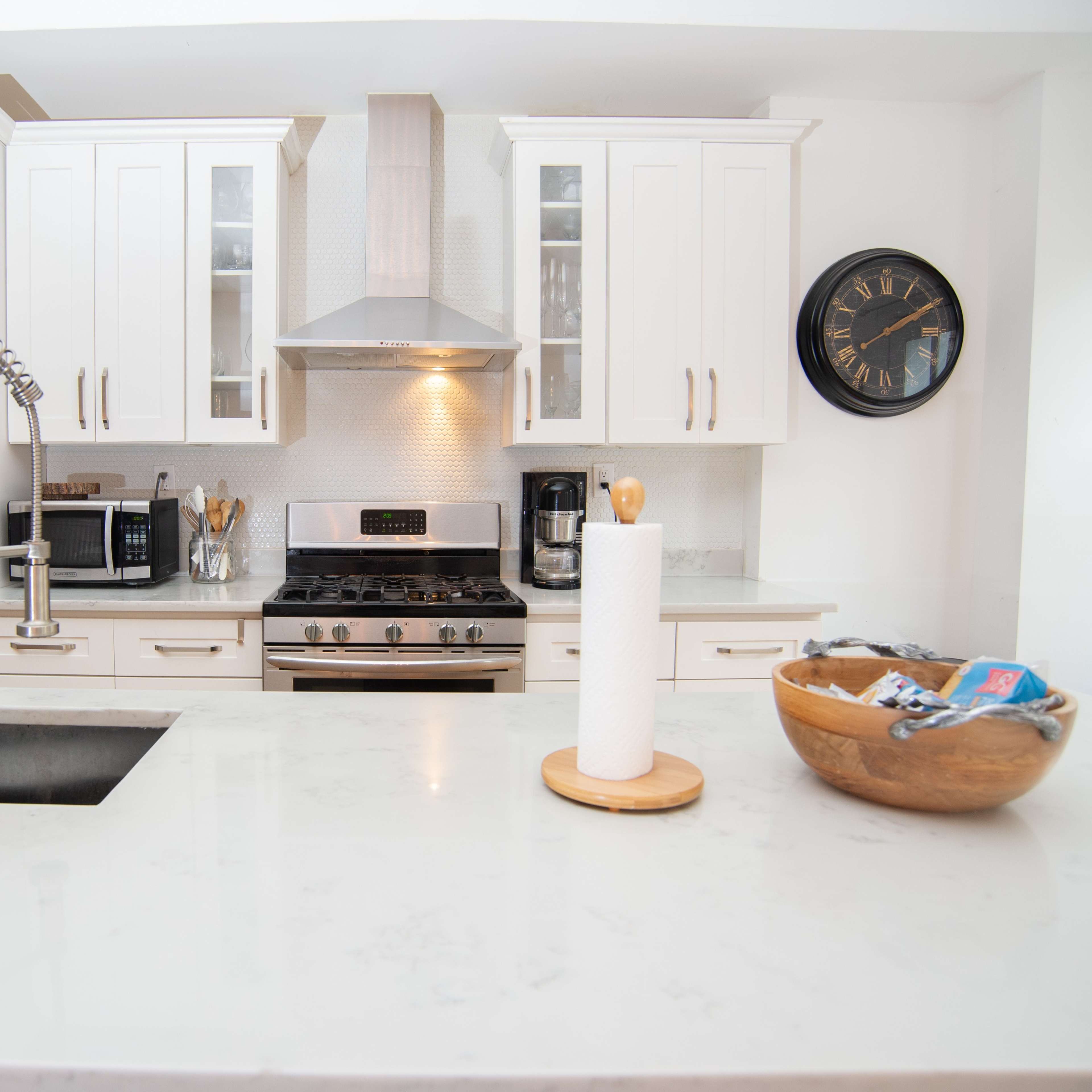 A modern kitchen with white cabinets, stainless steel appliances, a central island with a sink, and a wooden bowl on the counter.