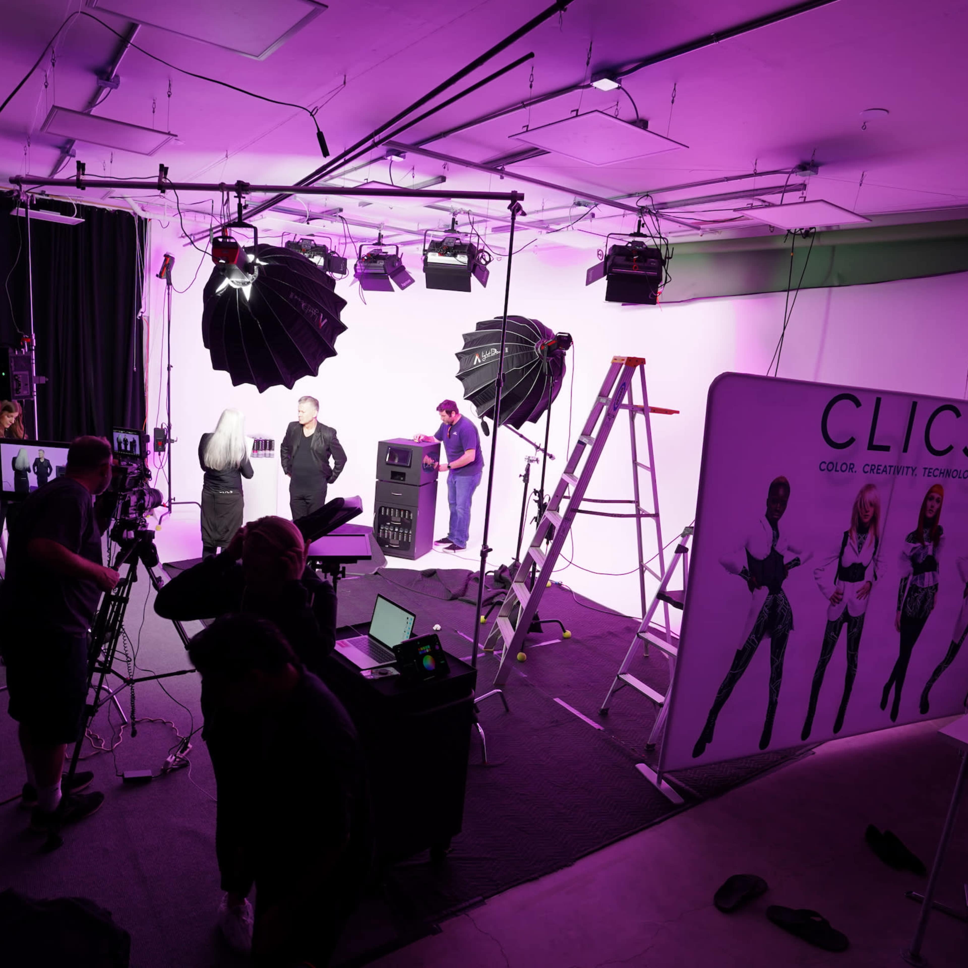 A photography studio setup features multiple lighting equipment, a large backdrop, and a team working on a photoshoot.