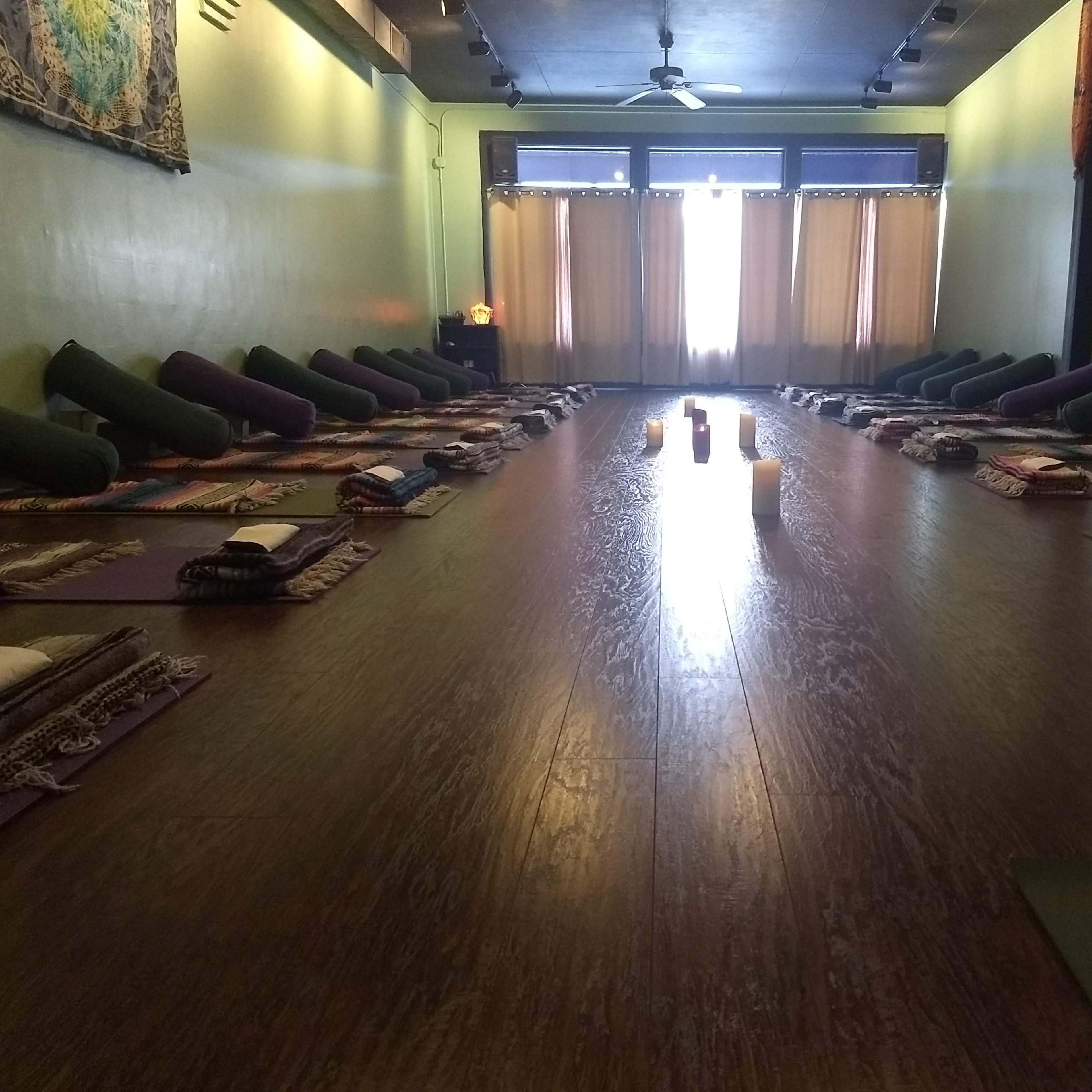 A yoga studio arranged with yoga mats and props in neat rows facing a large window with natural light.