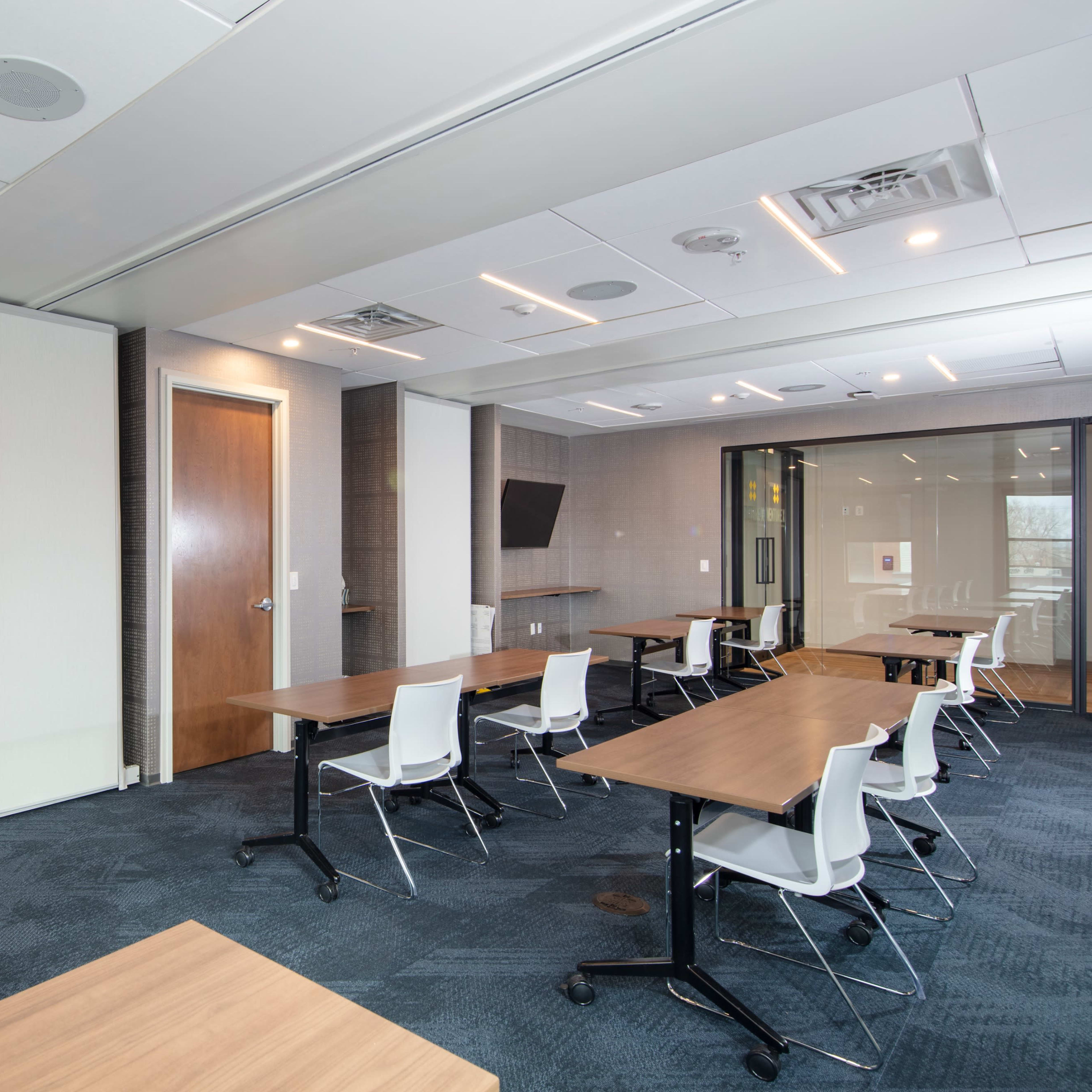 A modern conference room featuring several desks with chairs, wall-mounted televisions, and glass partitions.