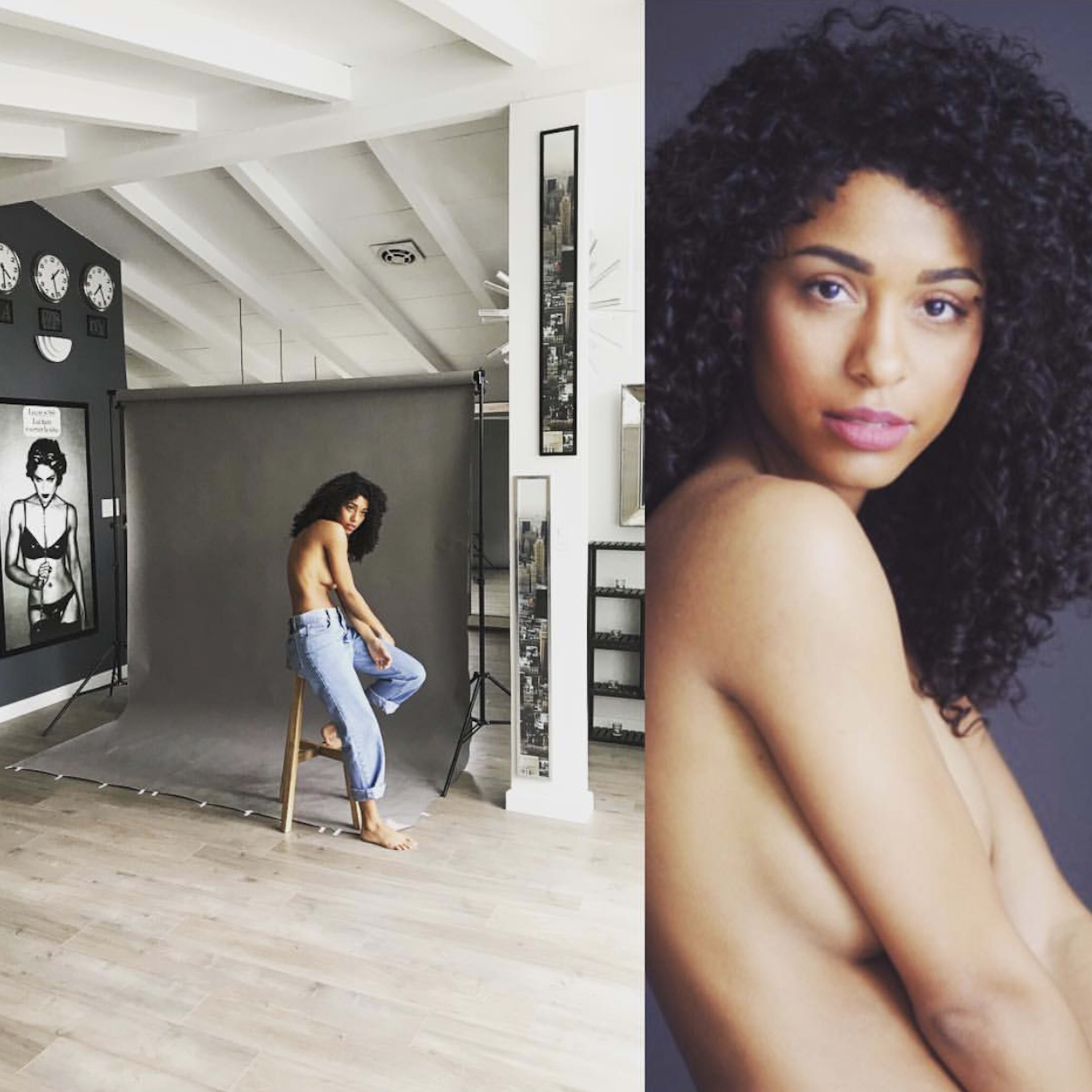 A woman with curly hair sits on a stool in a photography studio, facing a gray backdrop, while framed artwork and multiple clocks adorn the walls.
