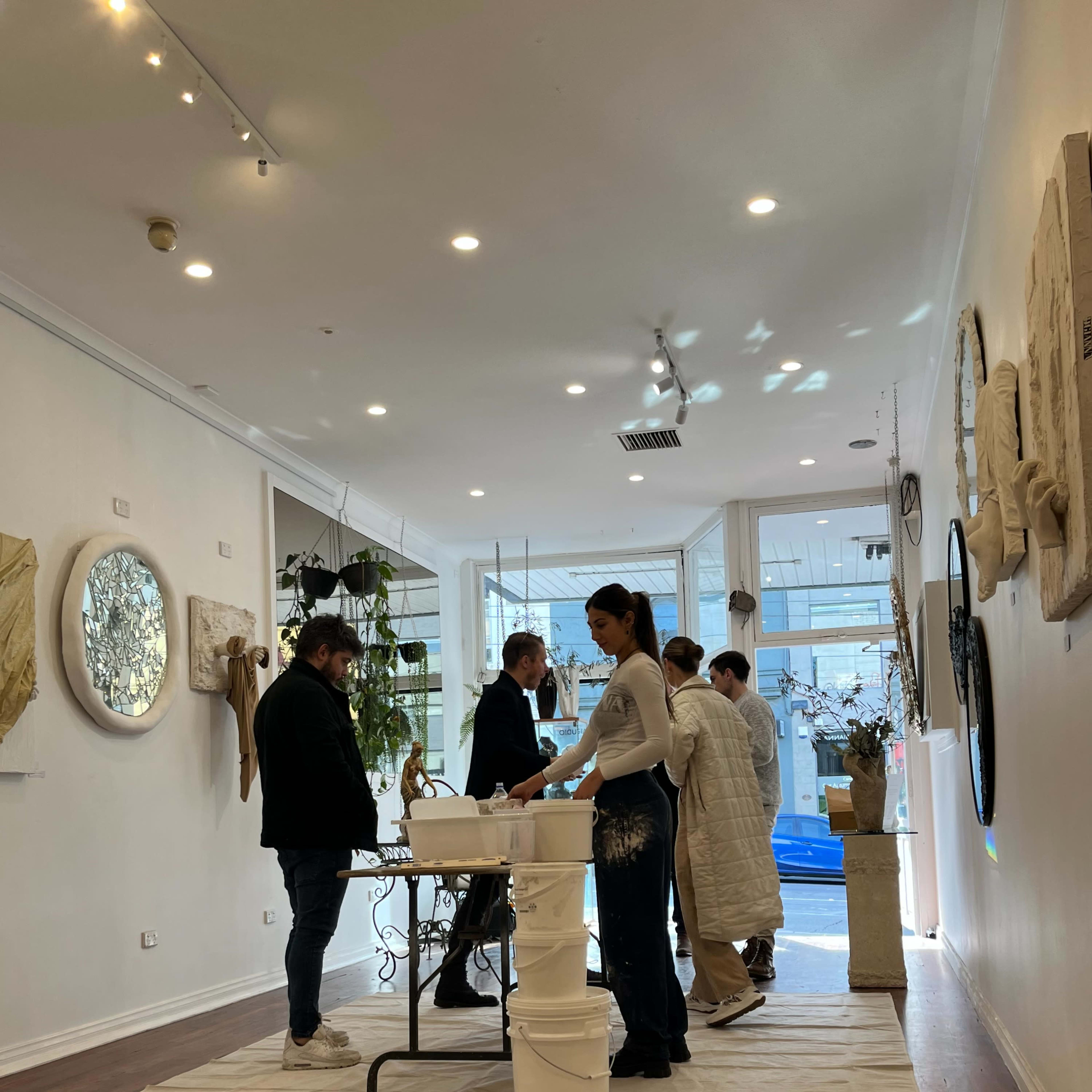 A group of five people engages in an activity inside a spacious art gallery with white walls and wooden flooring.