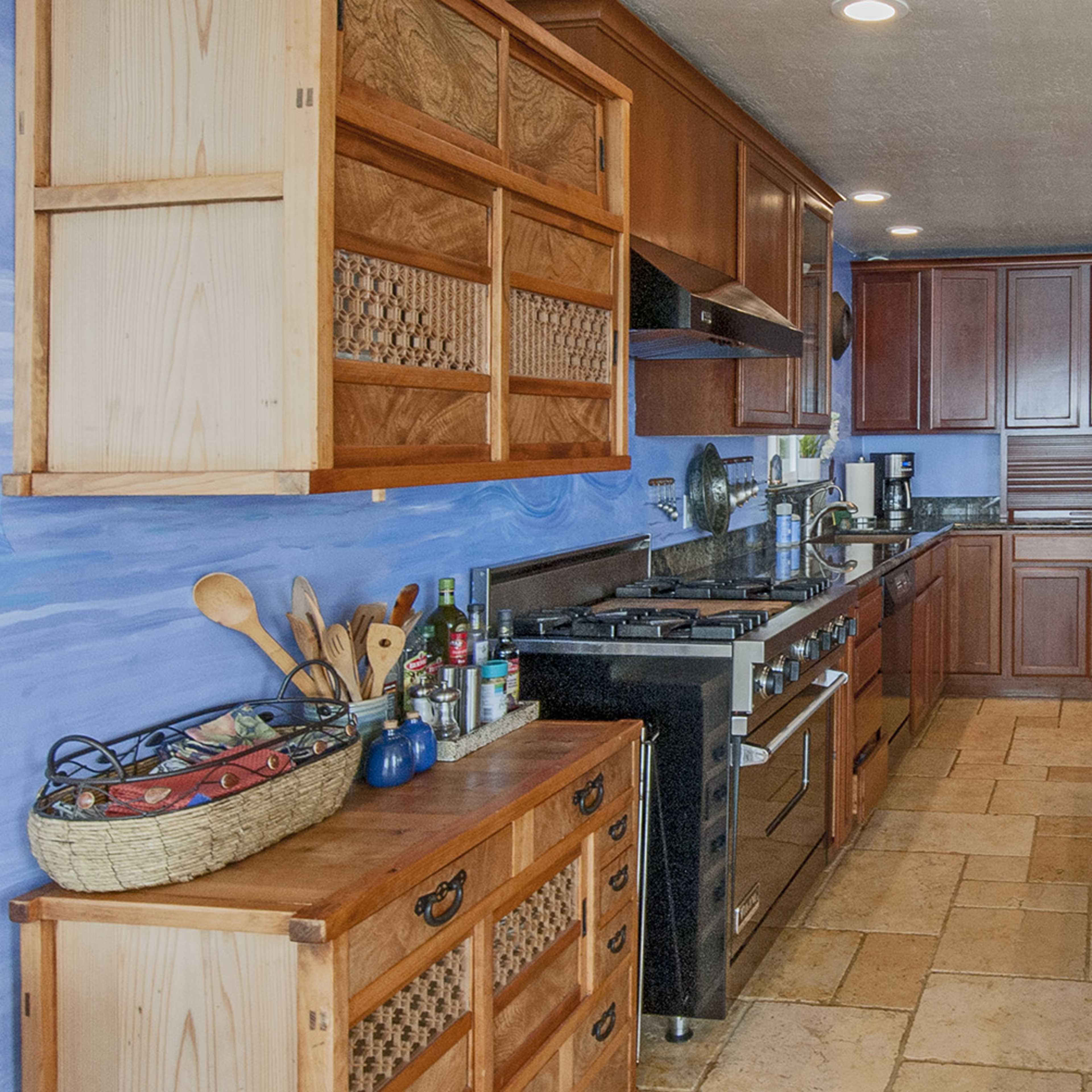 A modern kitchen with wooden cabinetry, a stainless steel stove, and a blue wall, featuring a countertop with various kitchen items and a vase of red flowers.