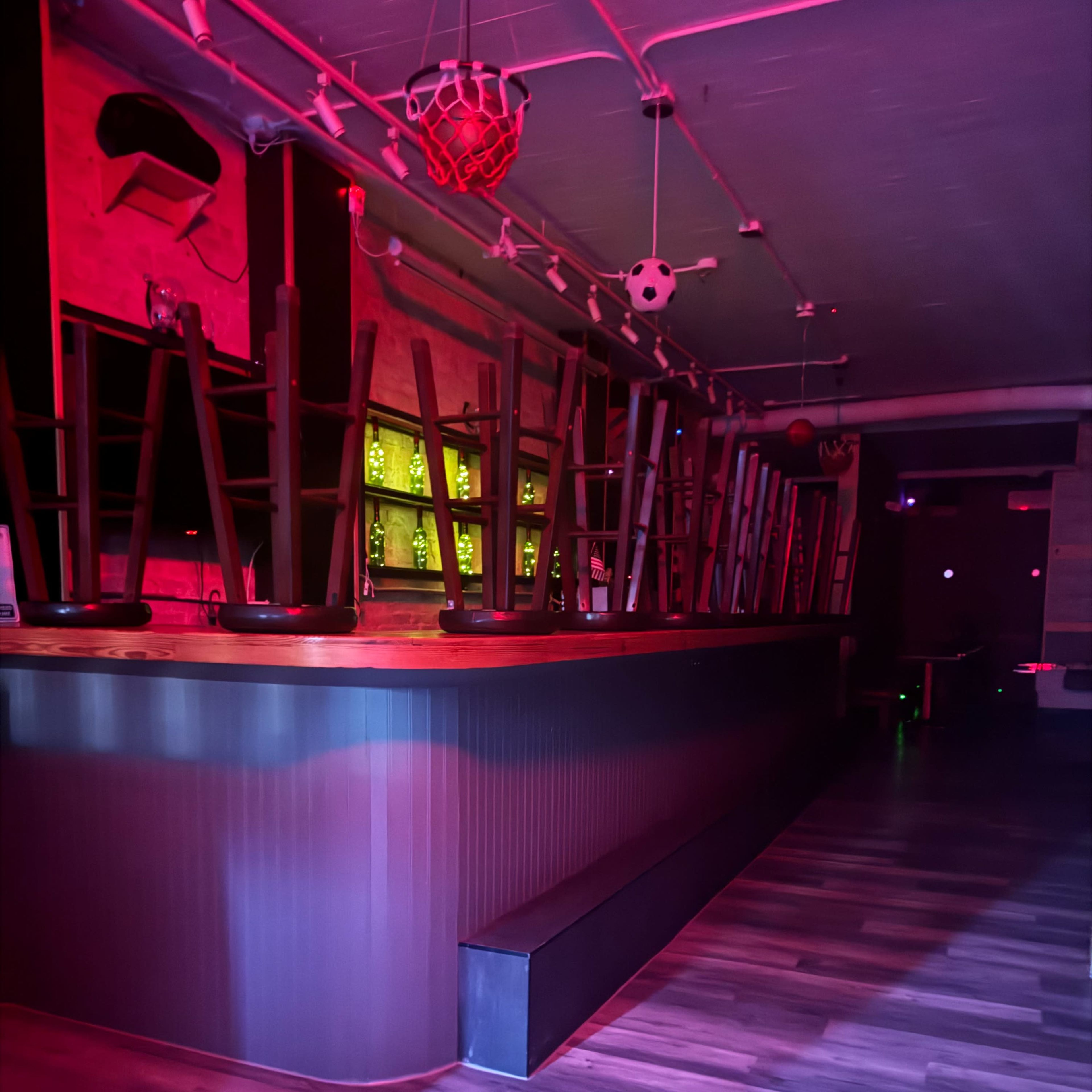 A dimly lit bar area with chairs stacked upside down on the counter and a wooden floor.
