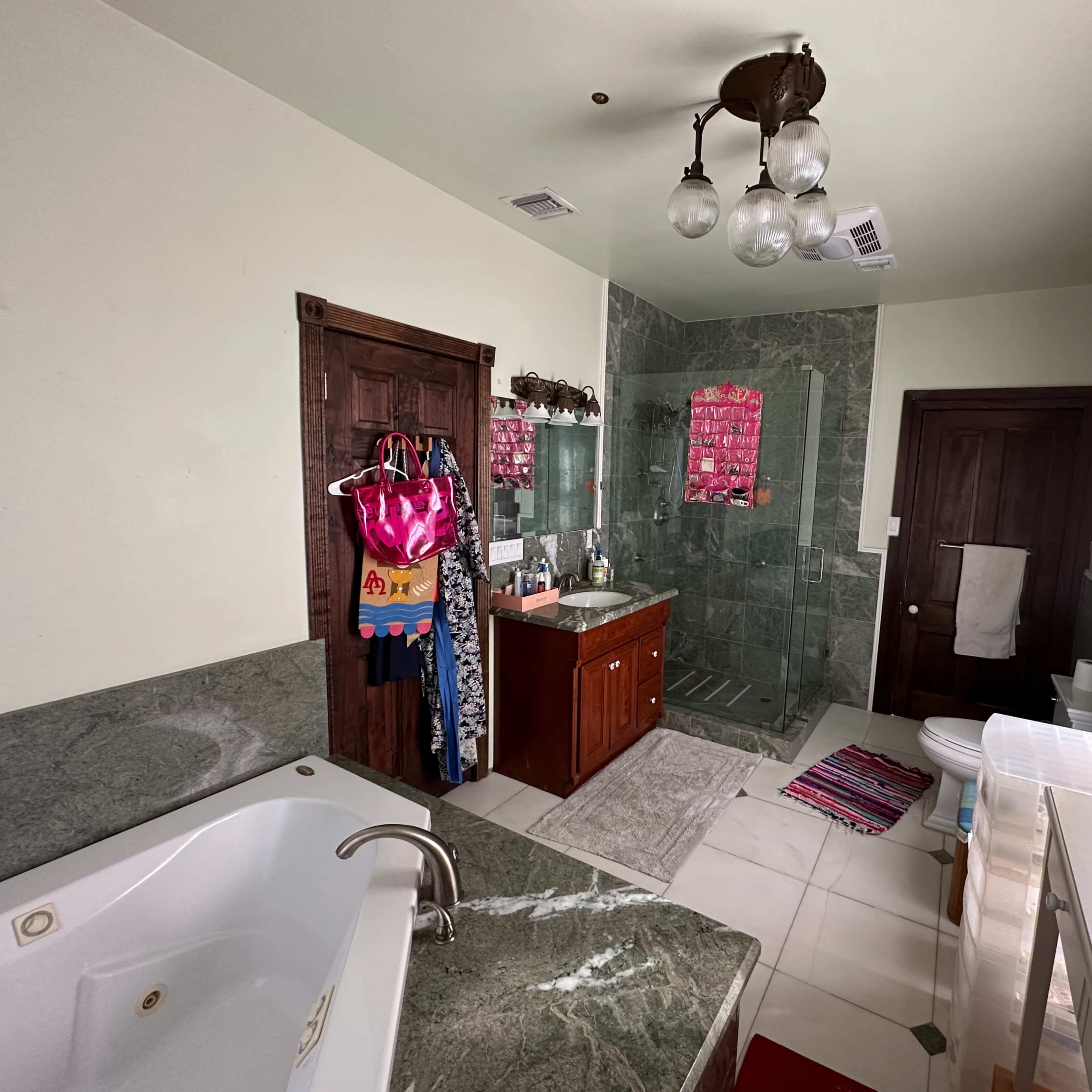 The bathroom features a granite countertop with a large bathtub, a wooden vanity, and a shower area enclosed by green tiles.
