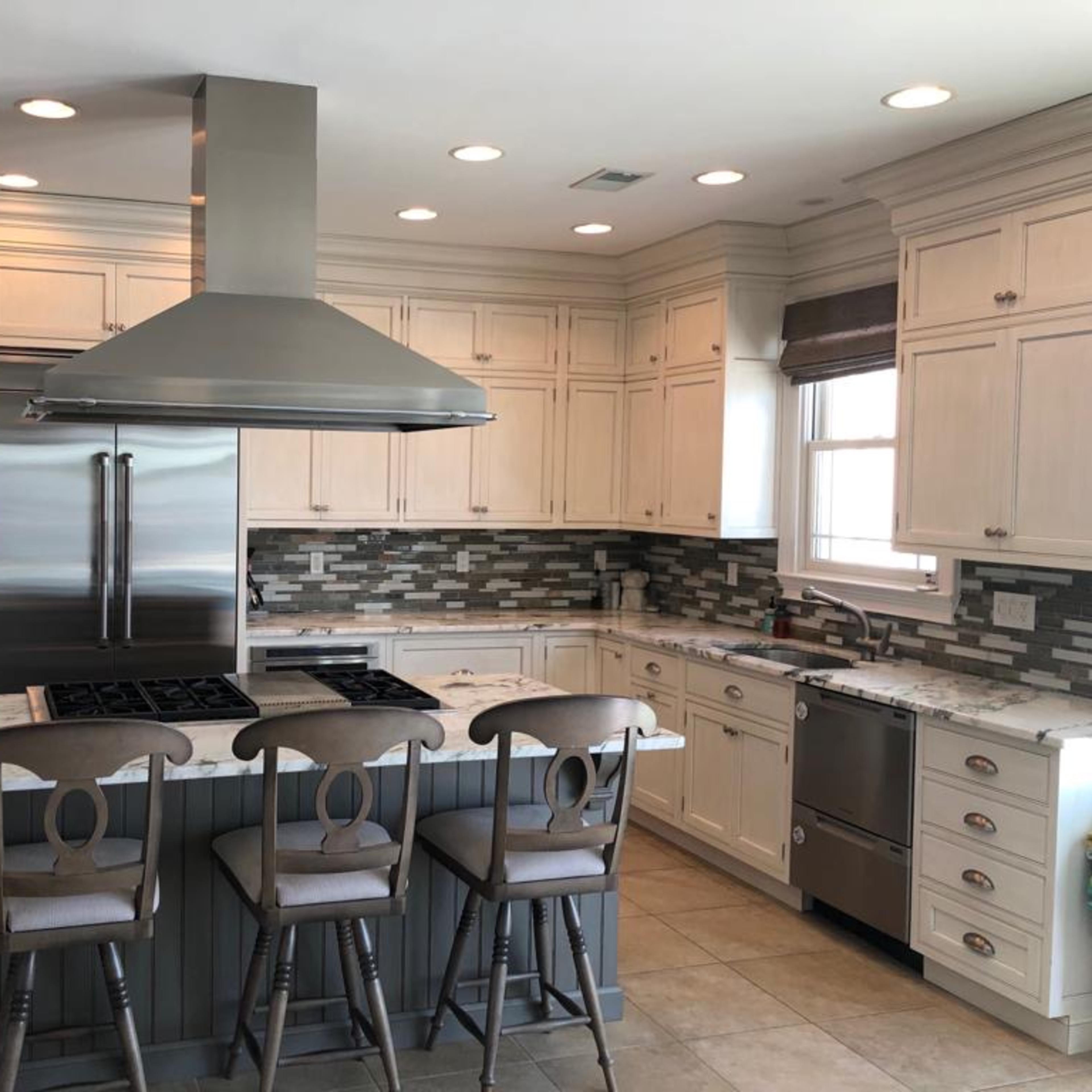 A modern kitchen featuring white cabinetry, a central island with bar stools, and stainless steel appliances.
