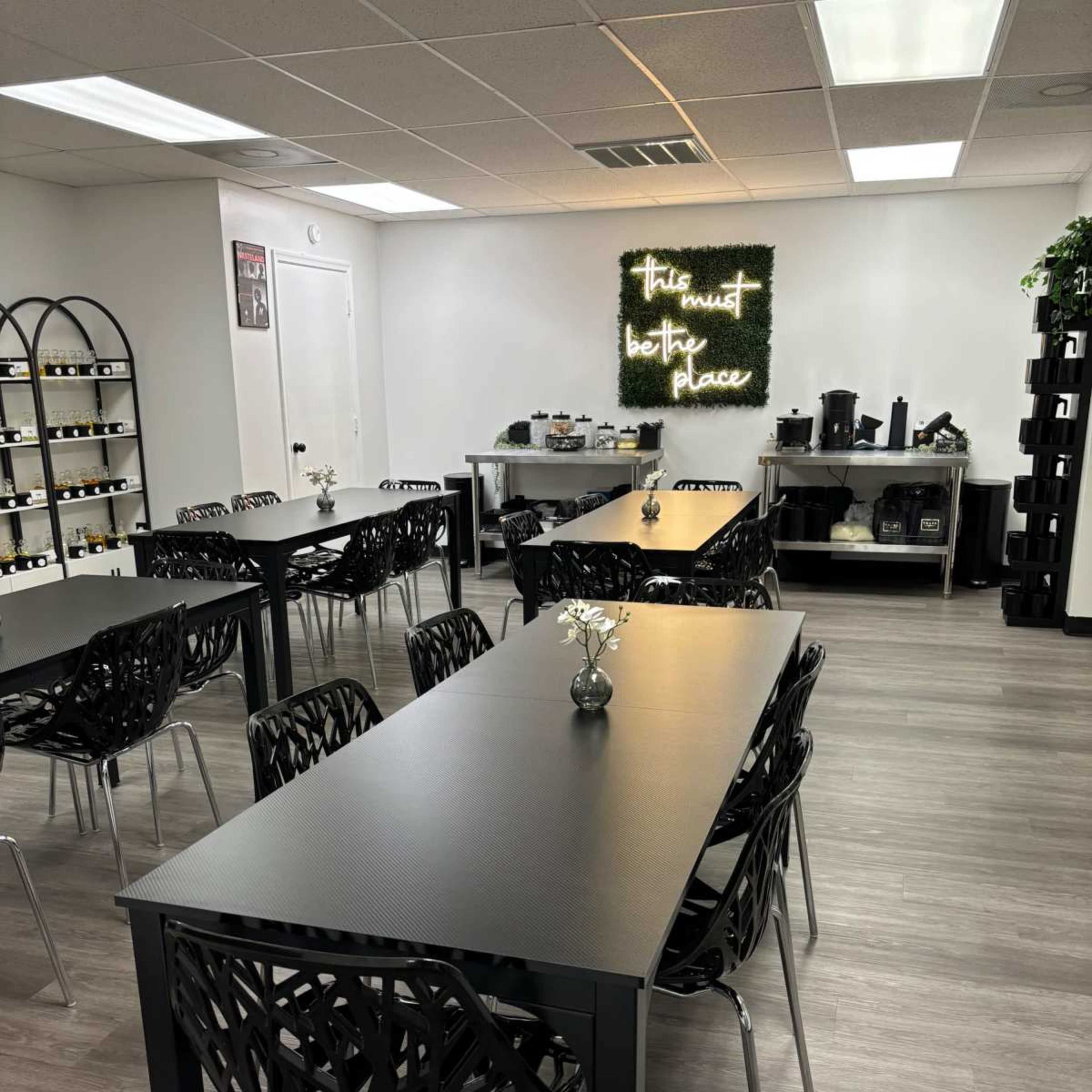 A neat room with several black tables and chairs arranged for a gathering, featuring a decorative wall with green lighting and plants.
