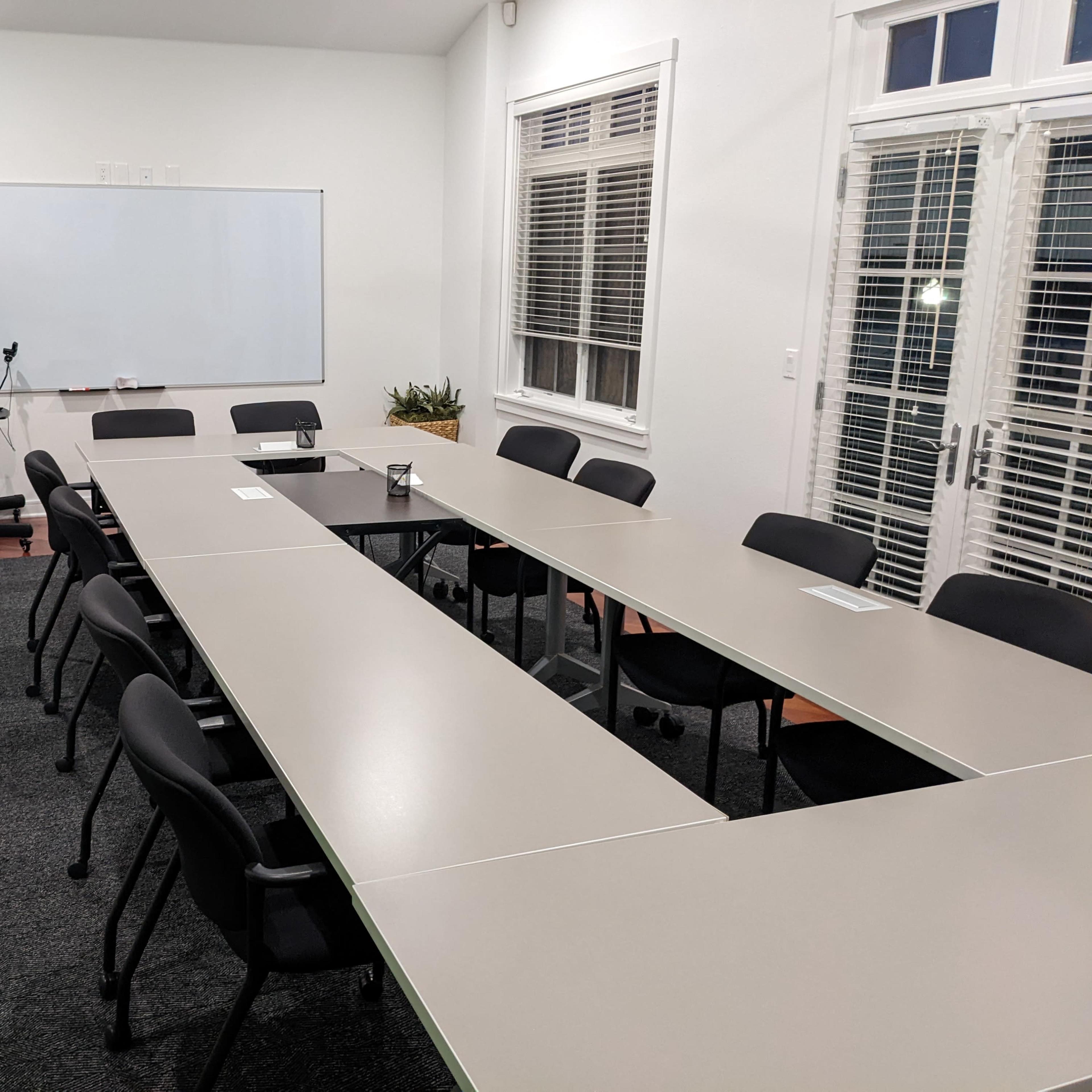 A conference room with a long rectangular table surrounded by chairs and a whiteboard at the front.