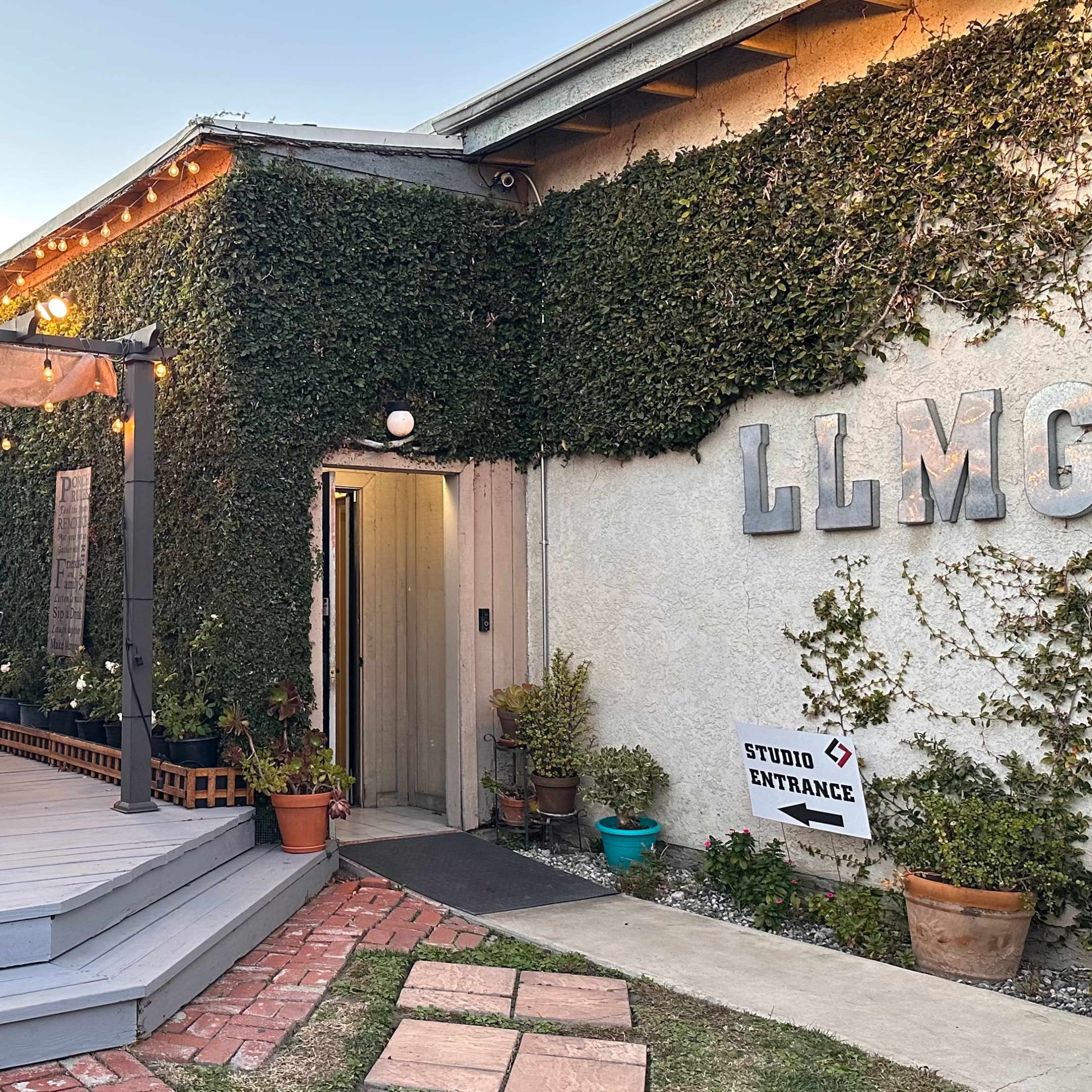 A building with an outdoor seating area, featuring a pergola covered in vines, and a sign indicating the studio entrance.