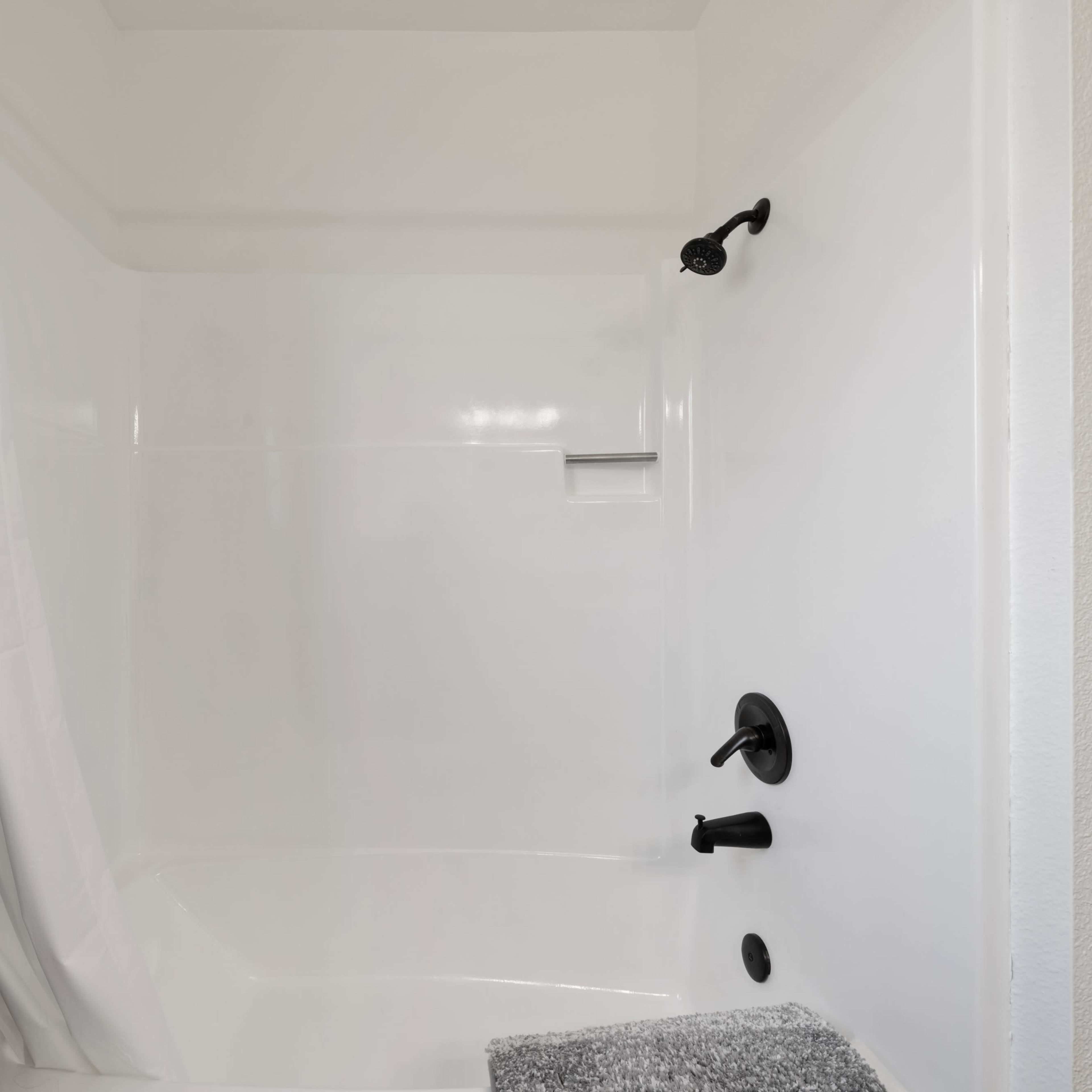 A clean, empty shower stall with a white interior, featuring black fixtures and a patterned curtain.
