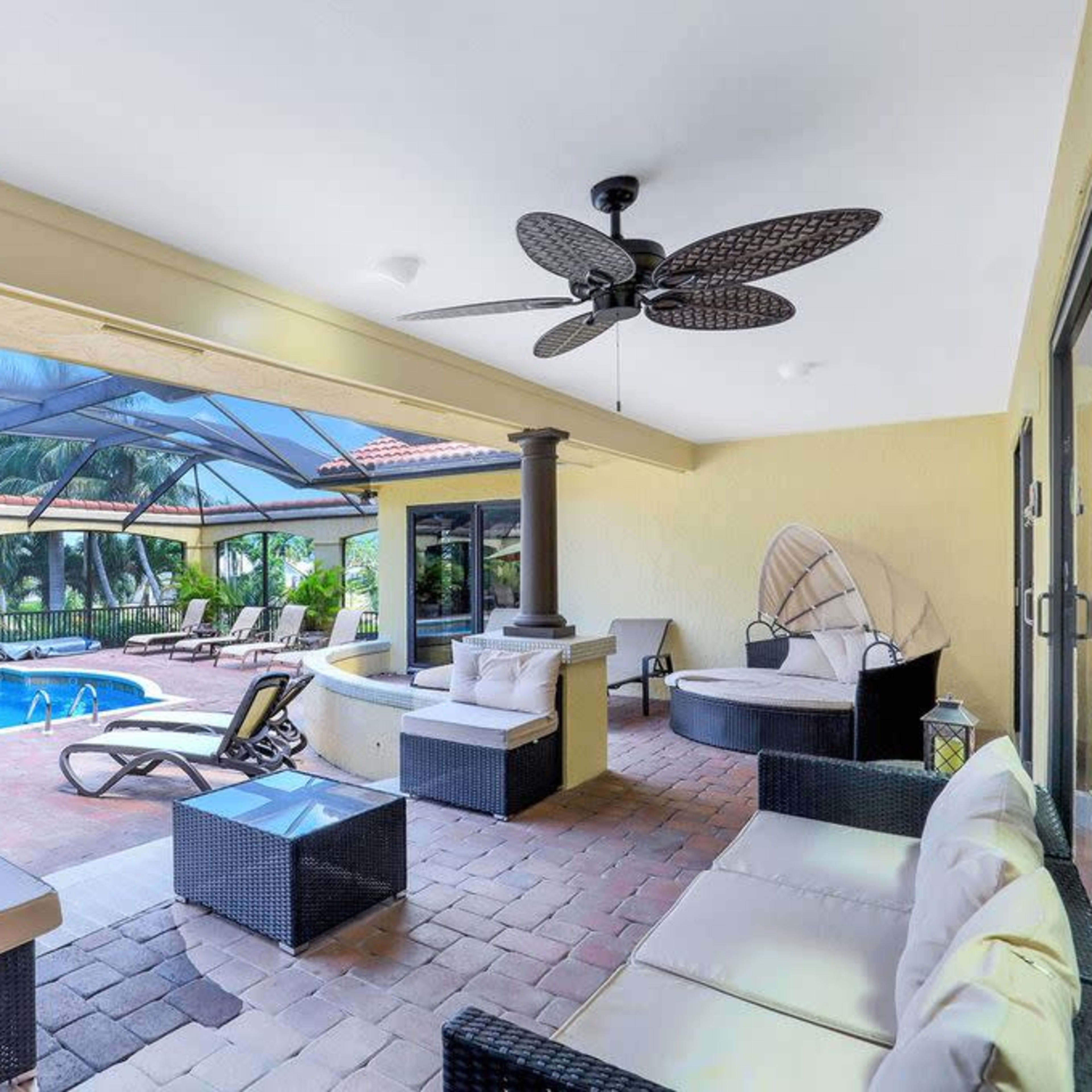 A covered outdoor patio with wicker furniture overlooking a swimming pool enclosed by a screen.
