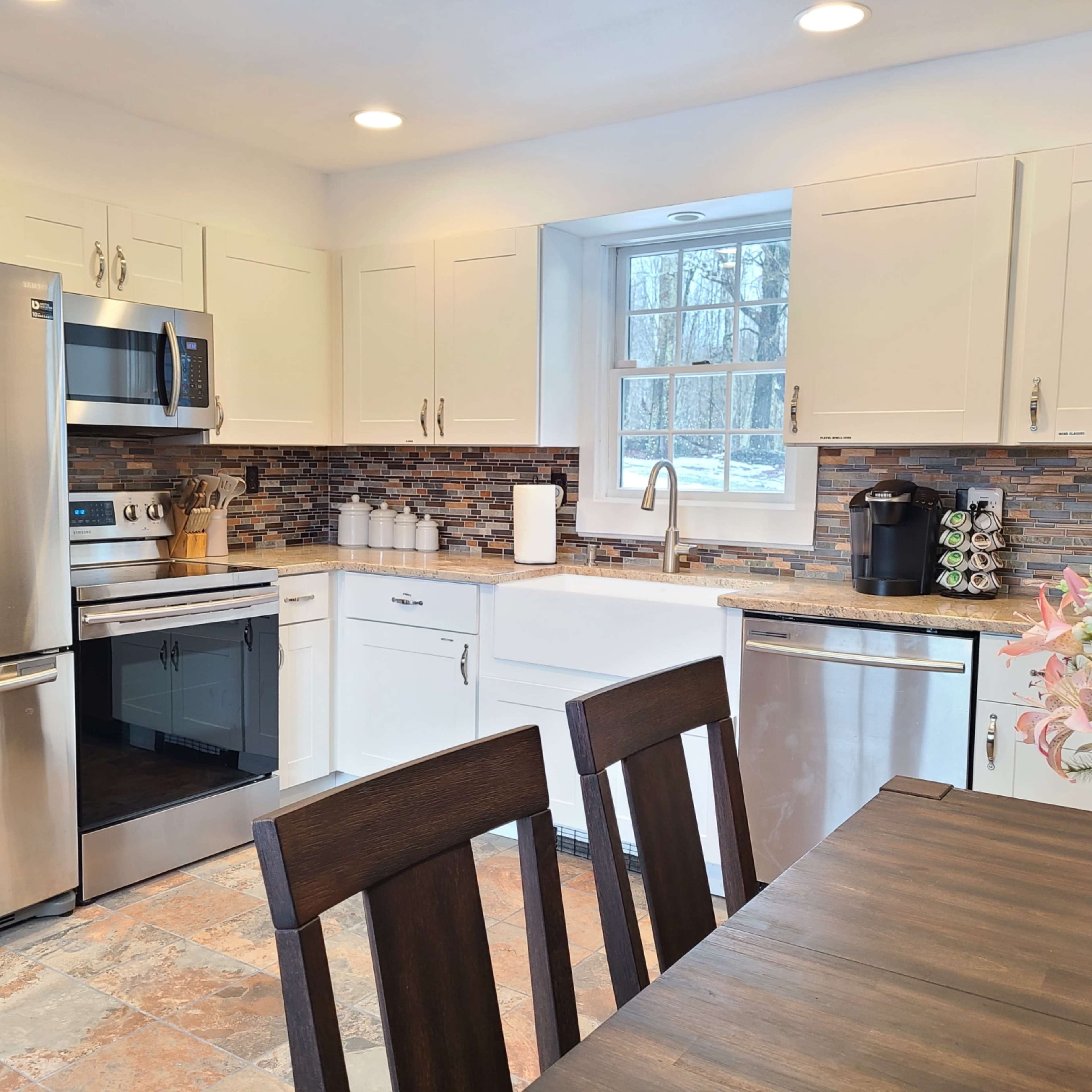 A modern kitchen with stainless steel appliances, white cabinetry, and a wooden dining table set for four.