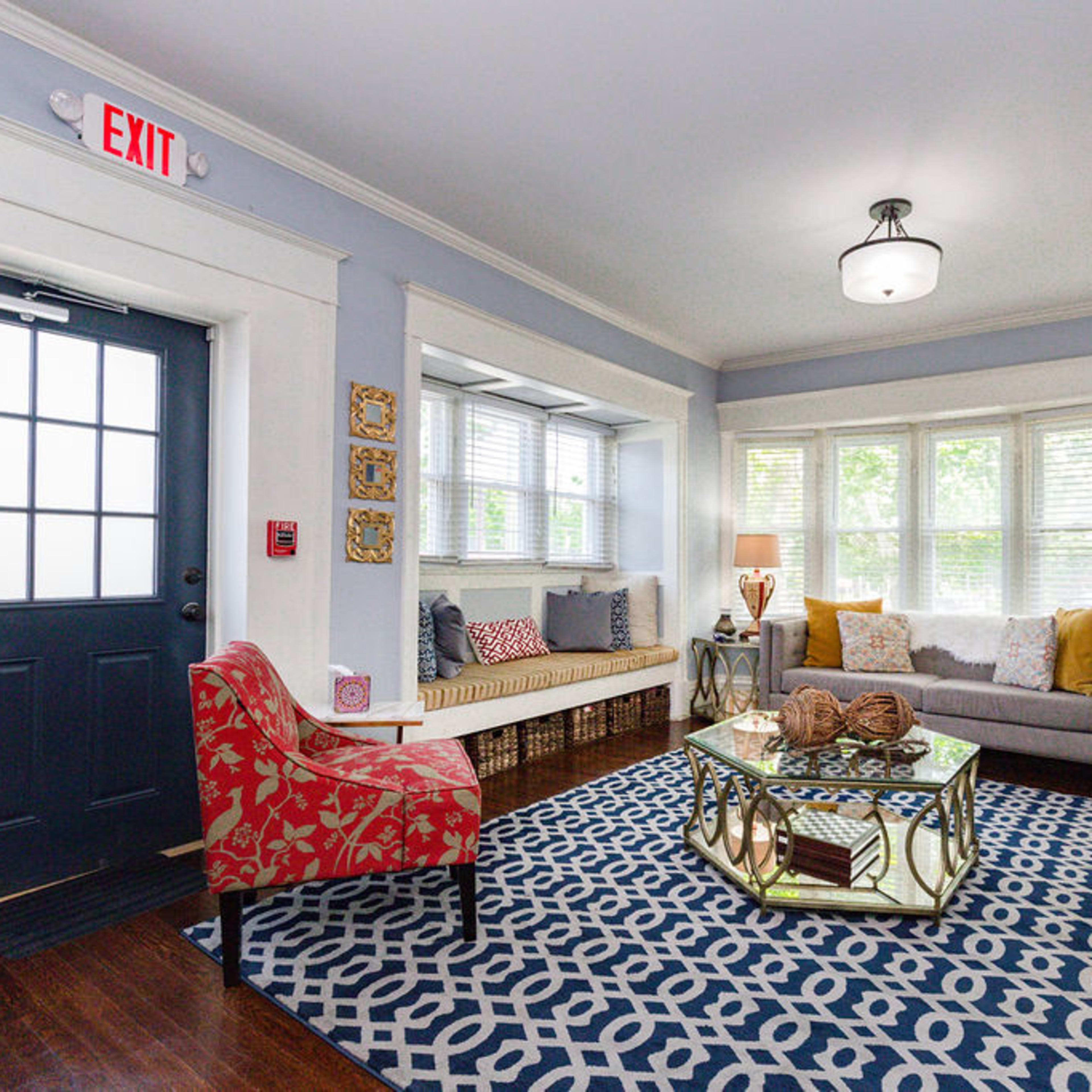 A cozy living room featuring a blue door, a patterned rug, a beige sofa with colorful cushions, and a coffee table surrounded by decorative items.