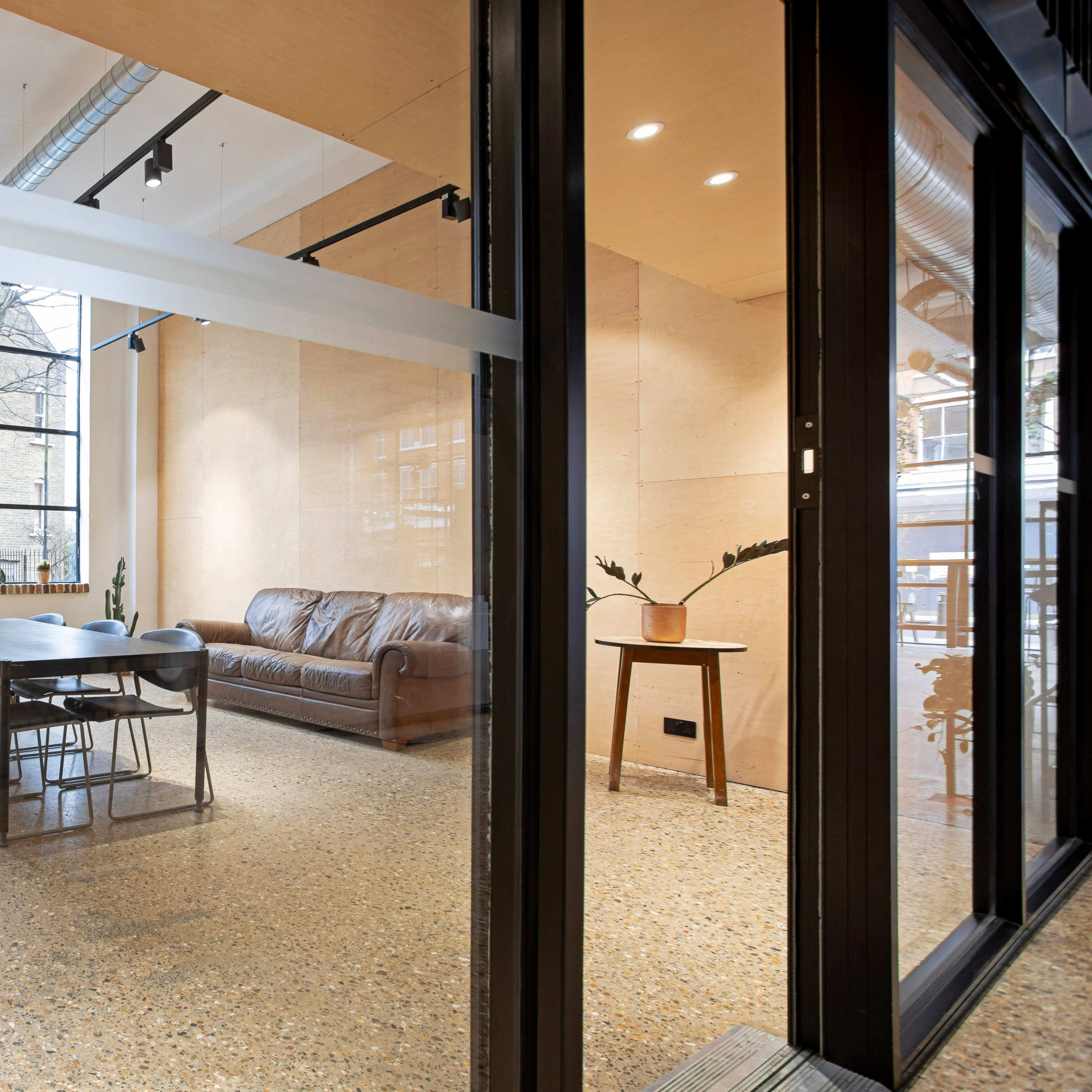 A modern, open-concept office space featuring a large window, a leather sofa, a dining table with chairs, and minimalist decor.