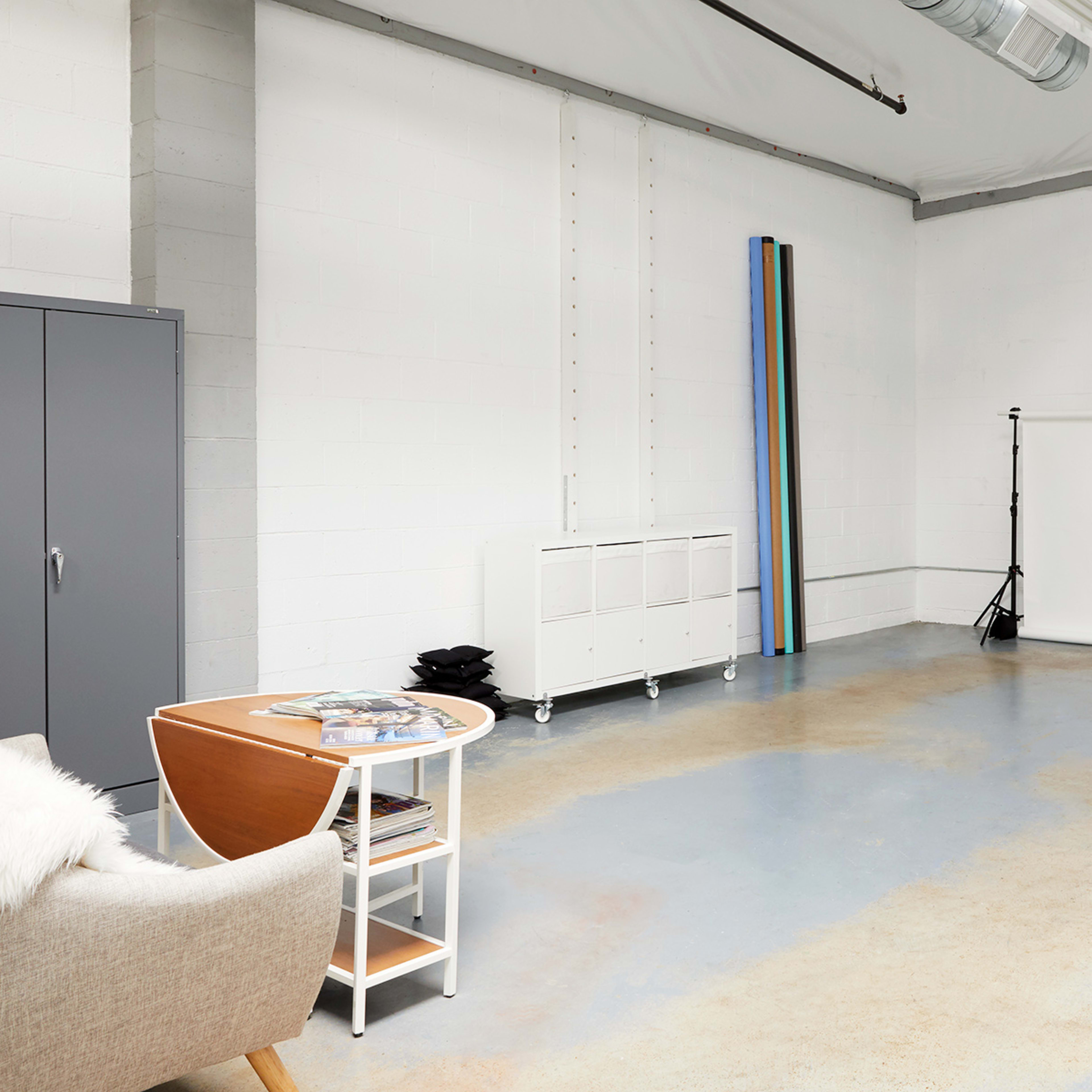 A spacious, empty studio with light gray walls and a white backdrop set up on stands, accompanied by a small table and a cabinet.