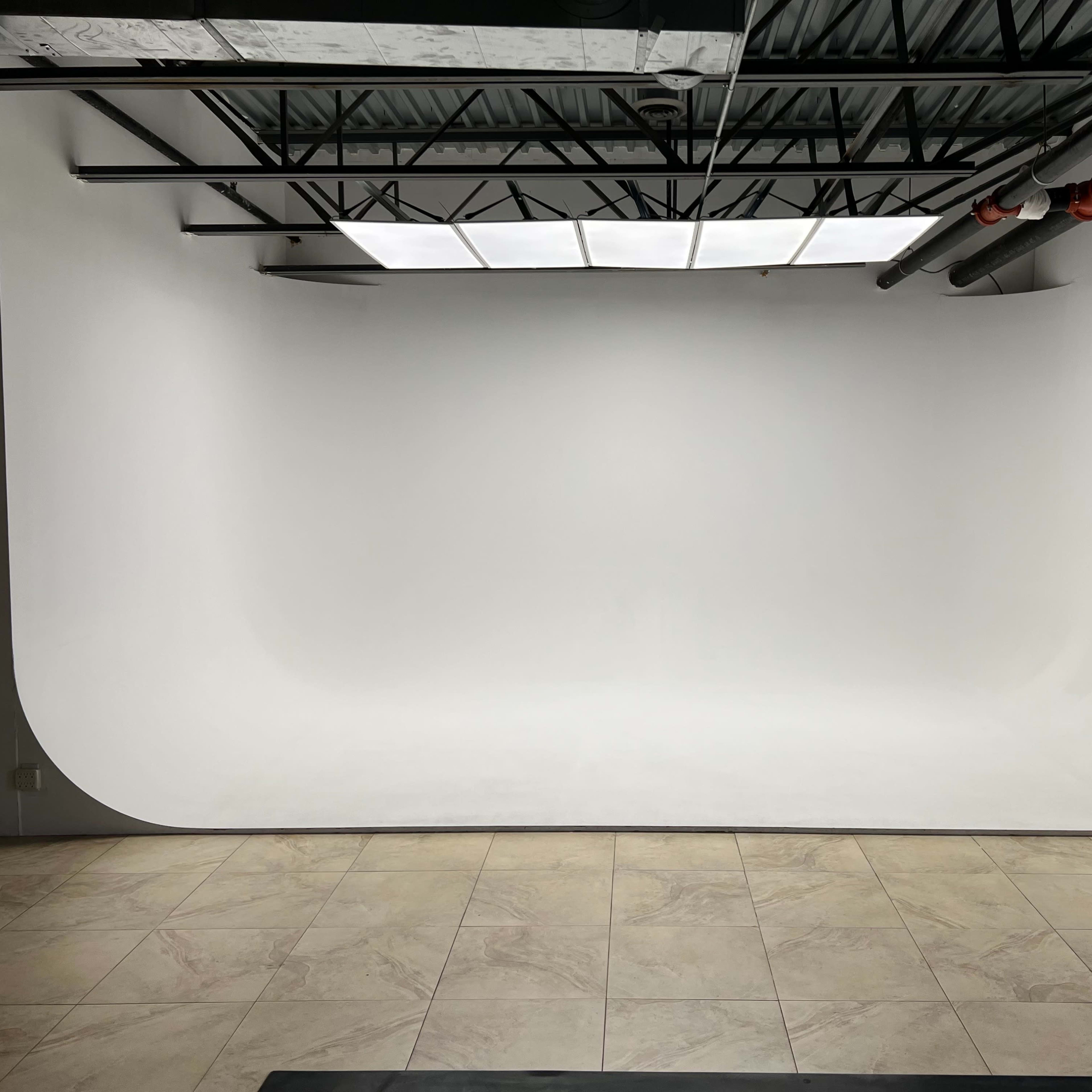 A studio space with a curved white backdrop against a neutral wall and tiled floor, illuminated by overhead lighting.