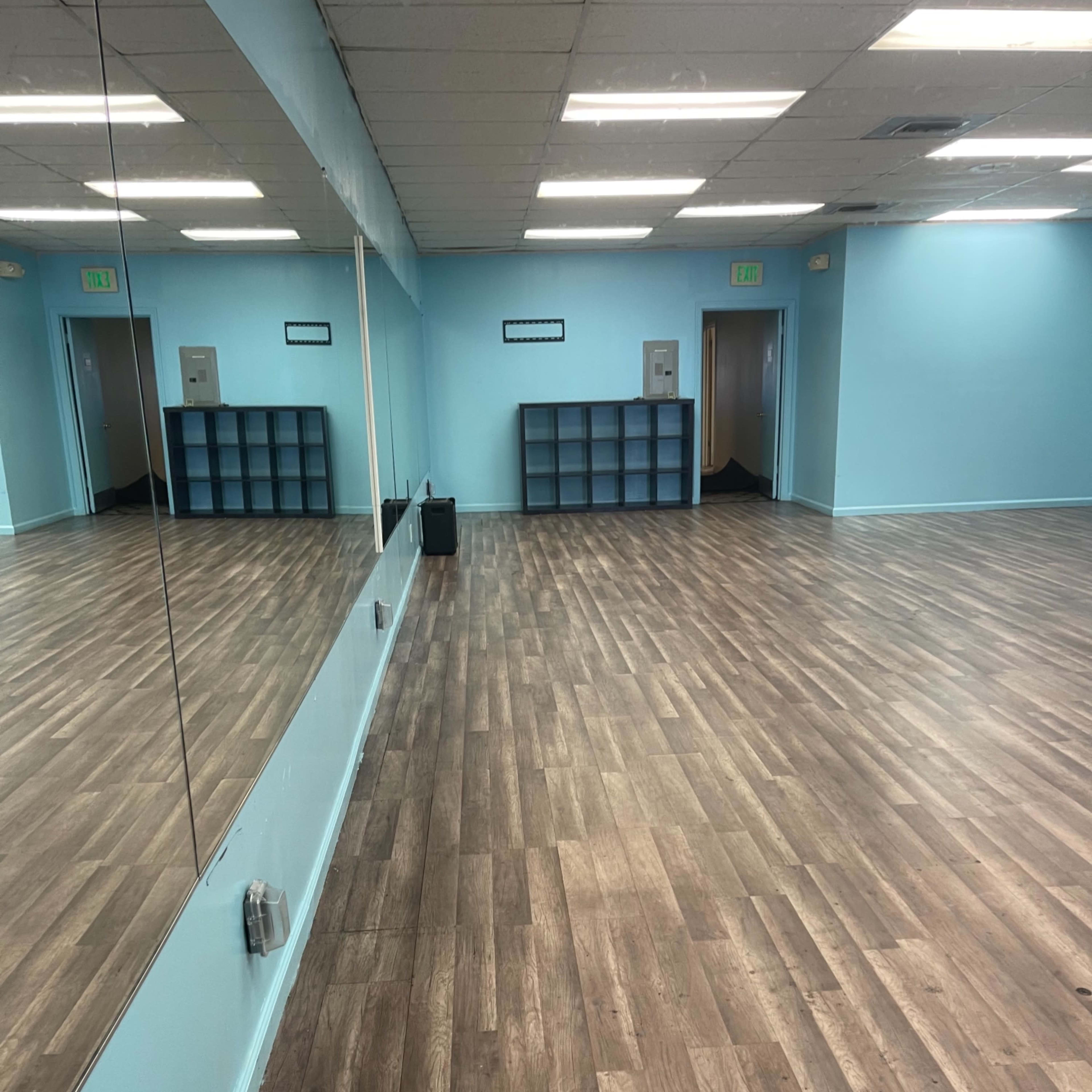 A spacious room with wooden flooring, light blue walls, and a large mirror along one side.