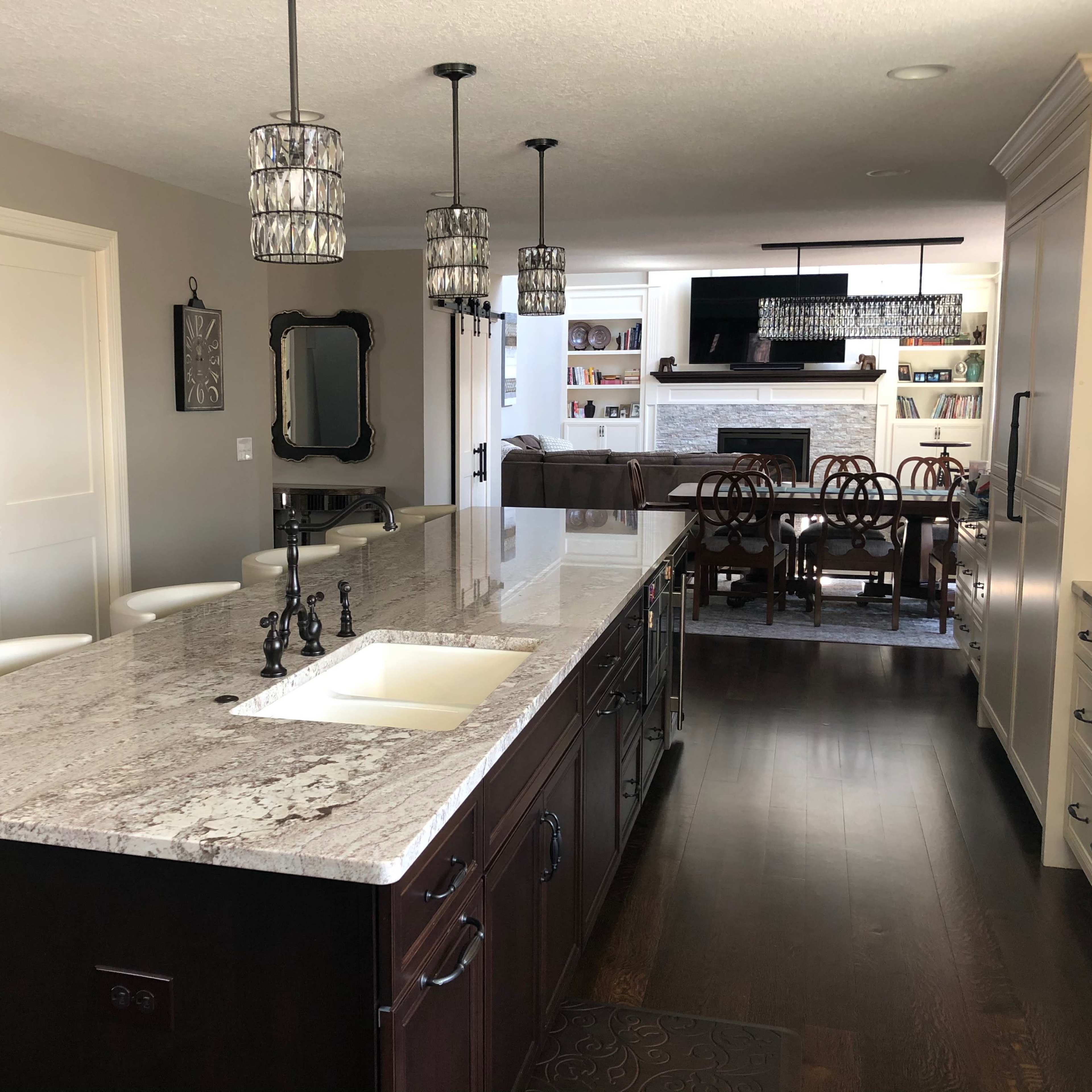 A modern kitchen with a large granite island, sleek cabinetry, and a view of a living room area in the background.