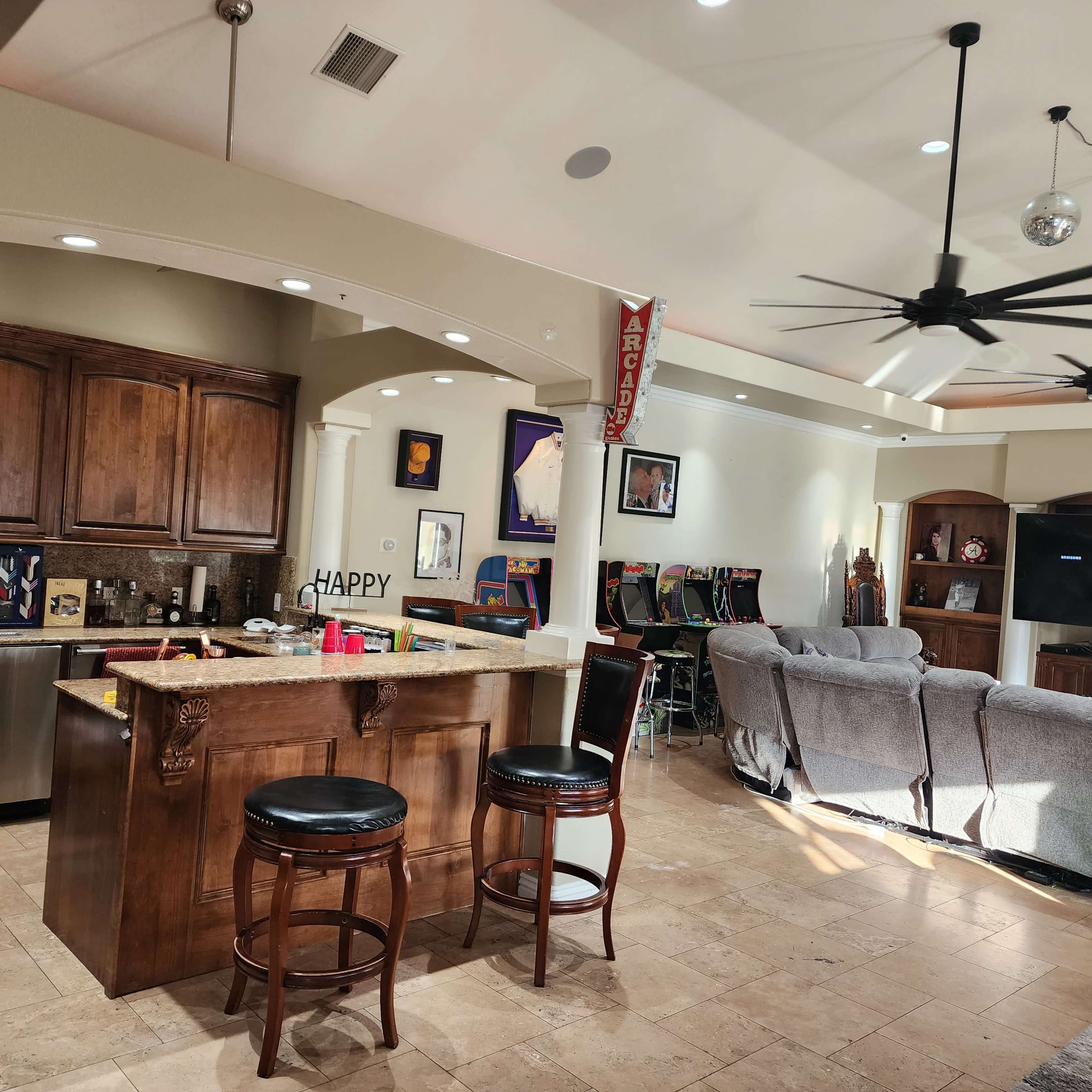 A spacious open-concept kitchen and living area featuring a bar counter with stools, wooden cabinetry, and a seating area with gray sofas.