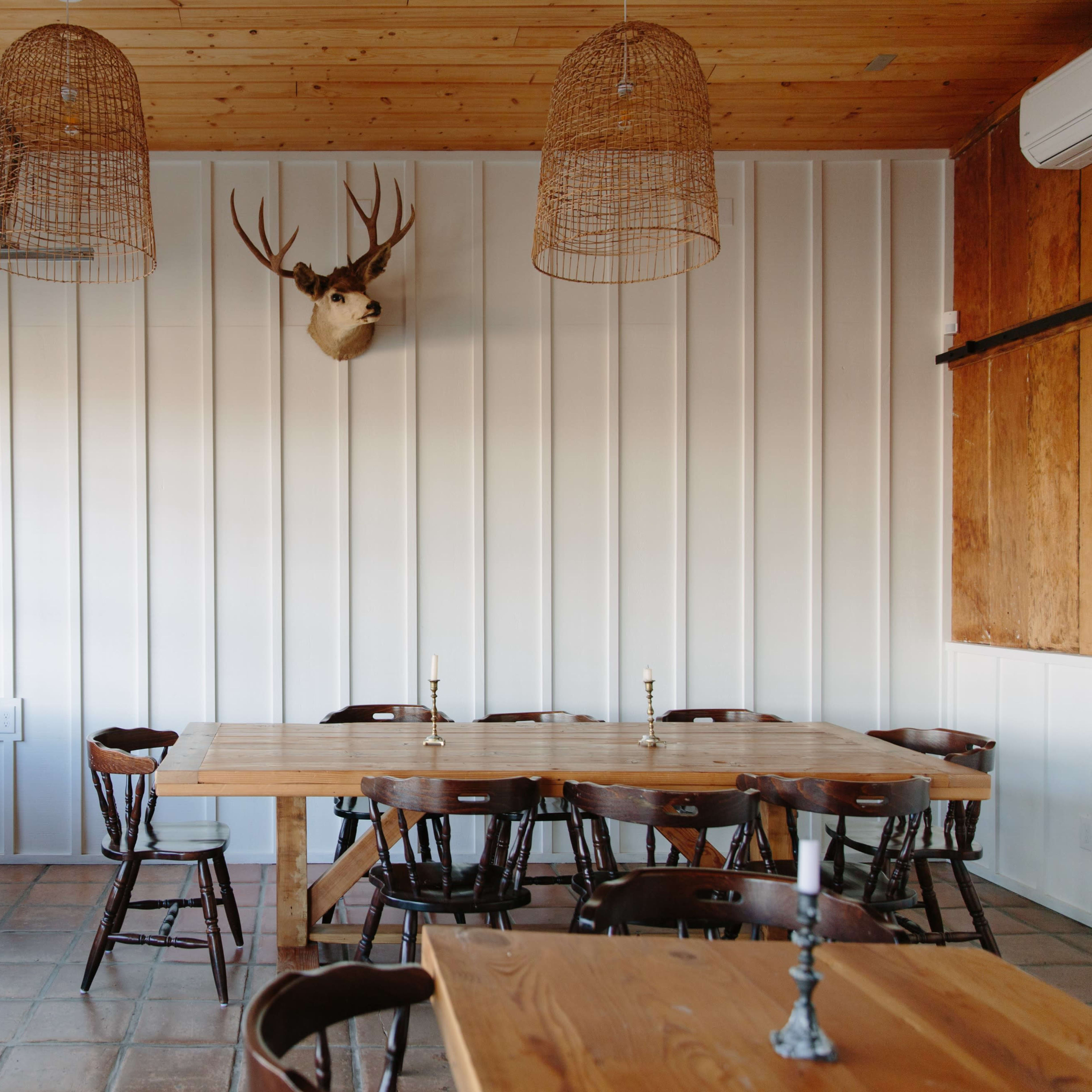 A spacious dining area features wooden tables, chairs, and a mounted deer head on the wall.